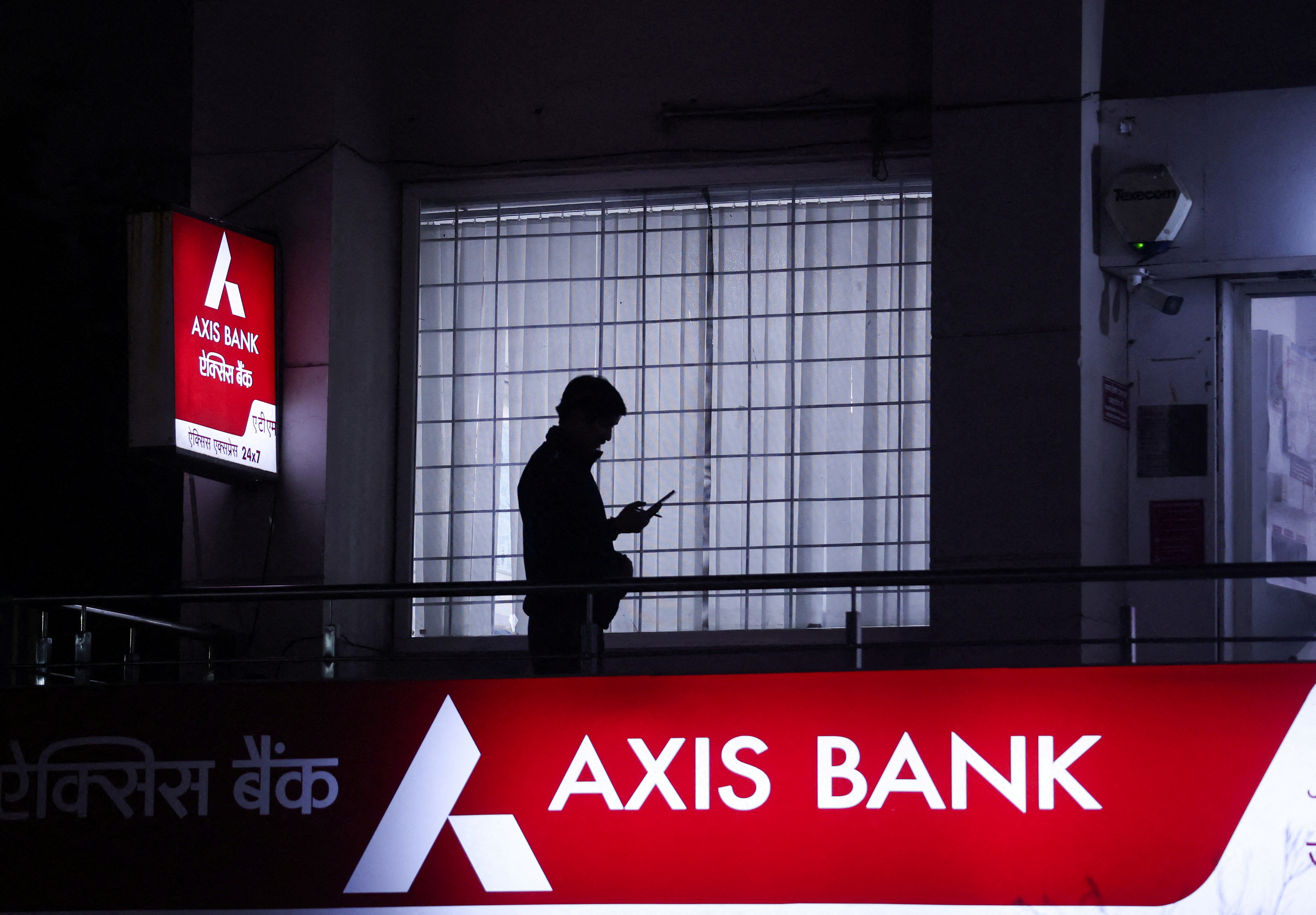 A person uses their mobile phone outside a branch of  Axis Bank in New Delhi