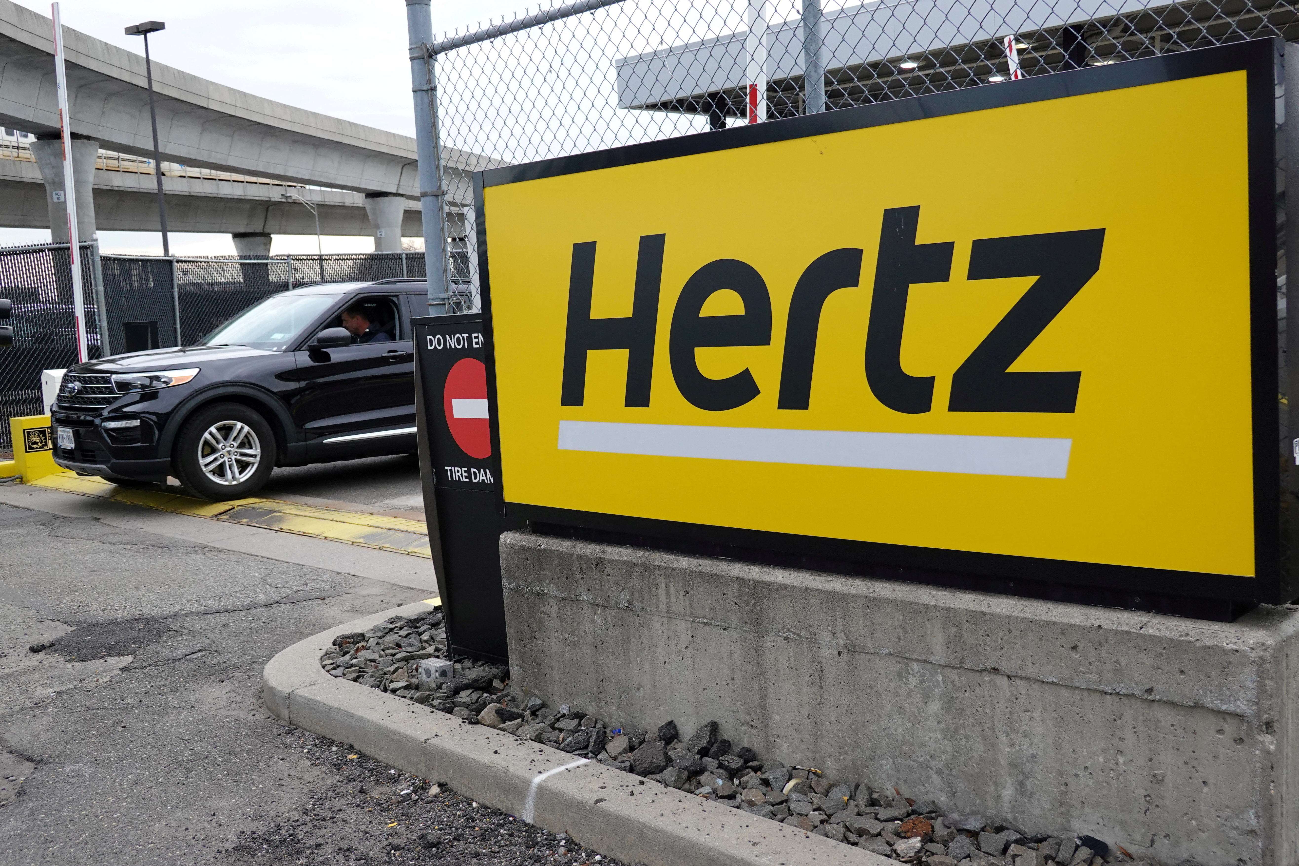 A car exits a lot and passes by Hertz rental car signage at John F. Kennedy International Airport in Queens, New York City