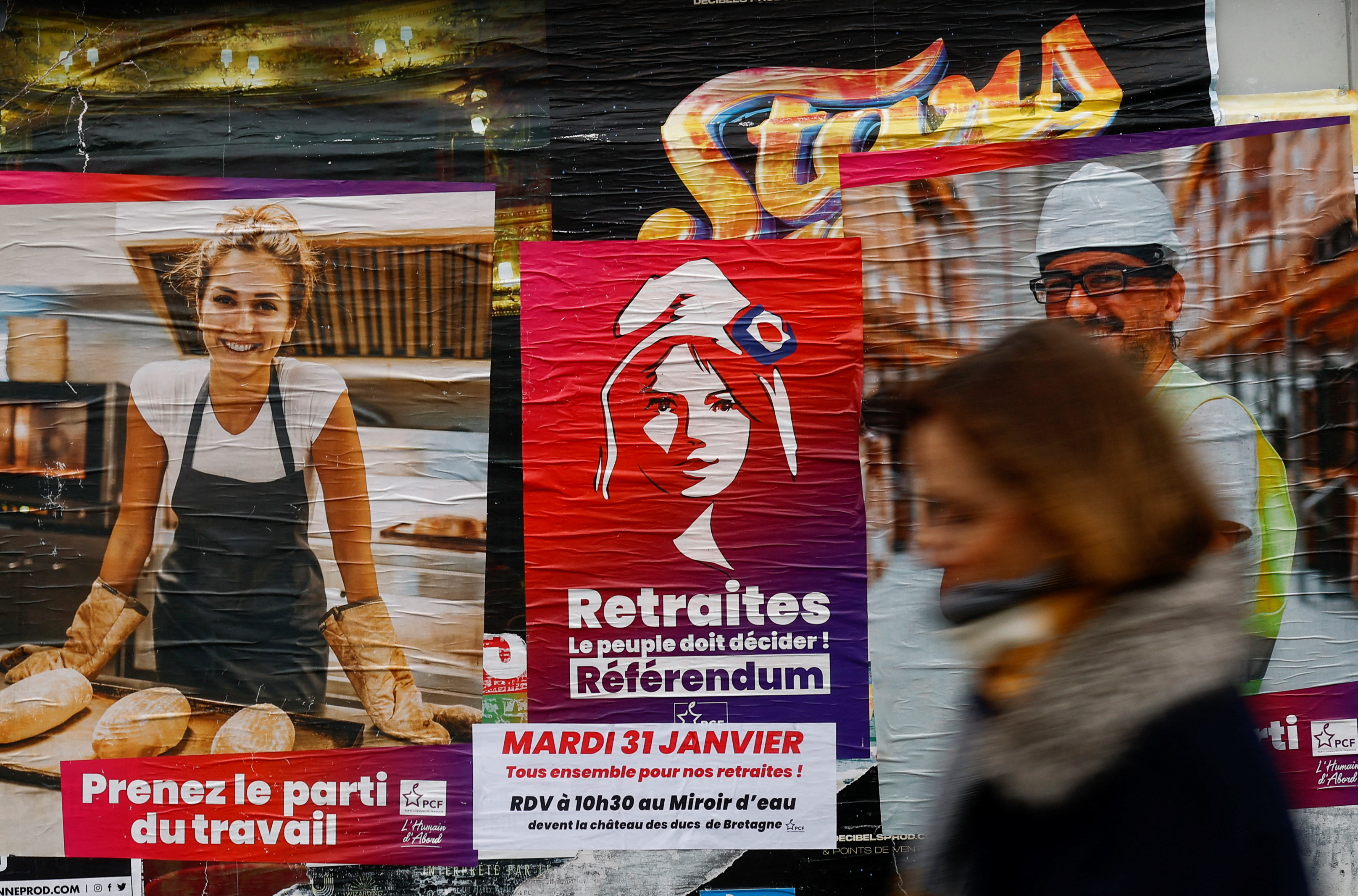 A woman walks in front of a poster calling for the demonstration against the pension reform in Reze