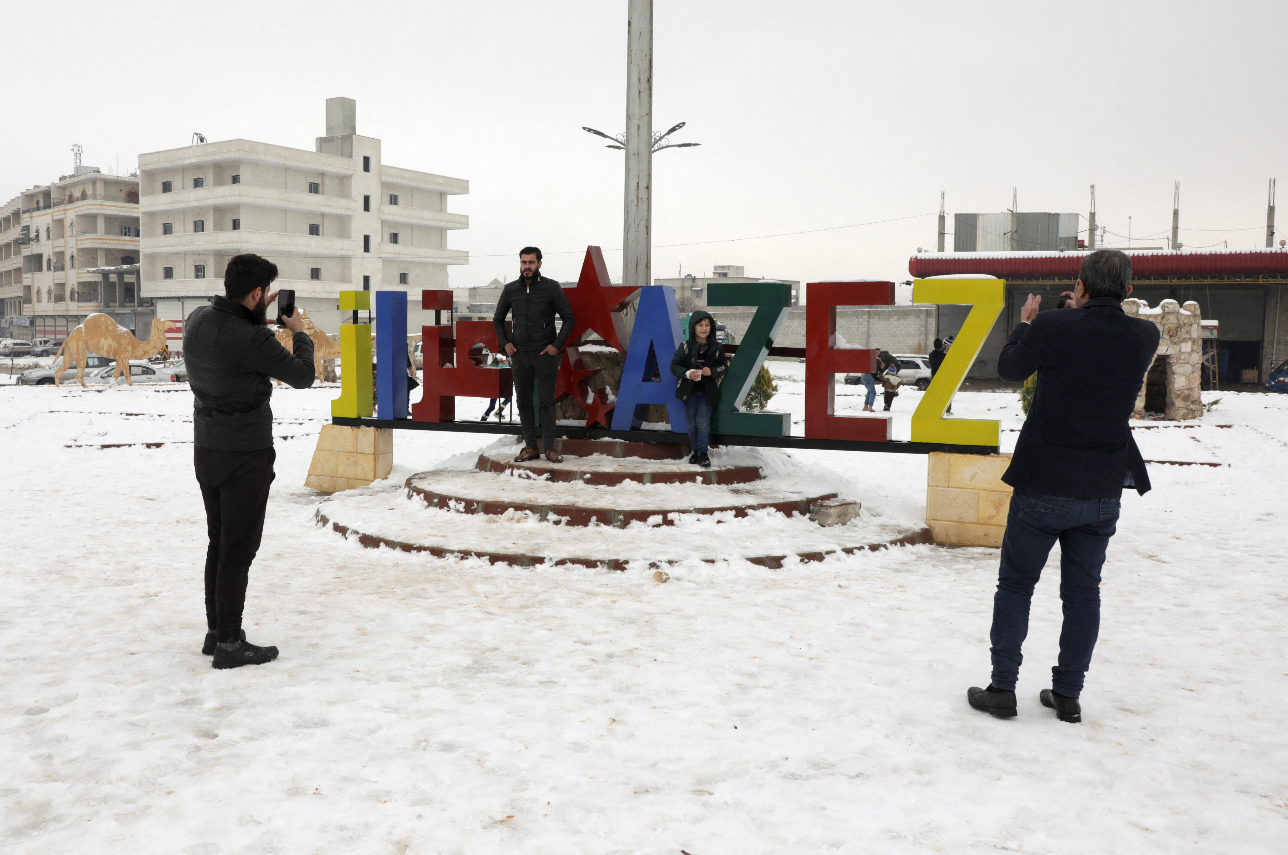 A man uses a mobile phone to take a picture of another man in the snow covered city of Azaz