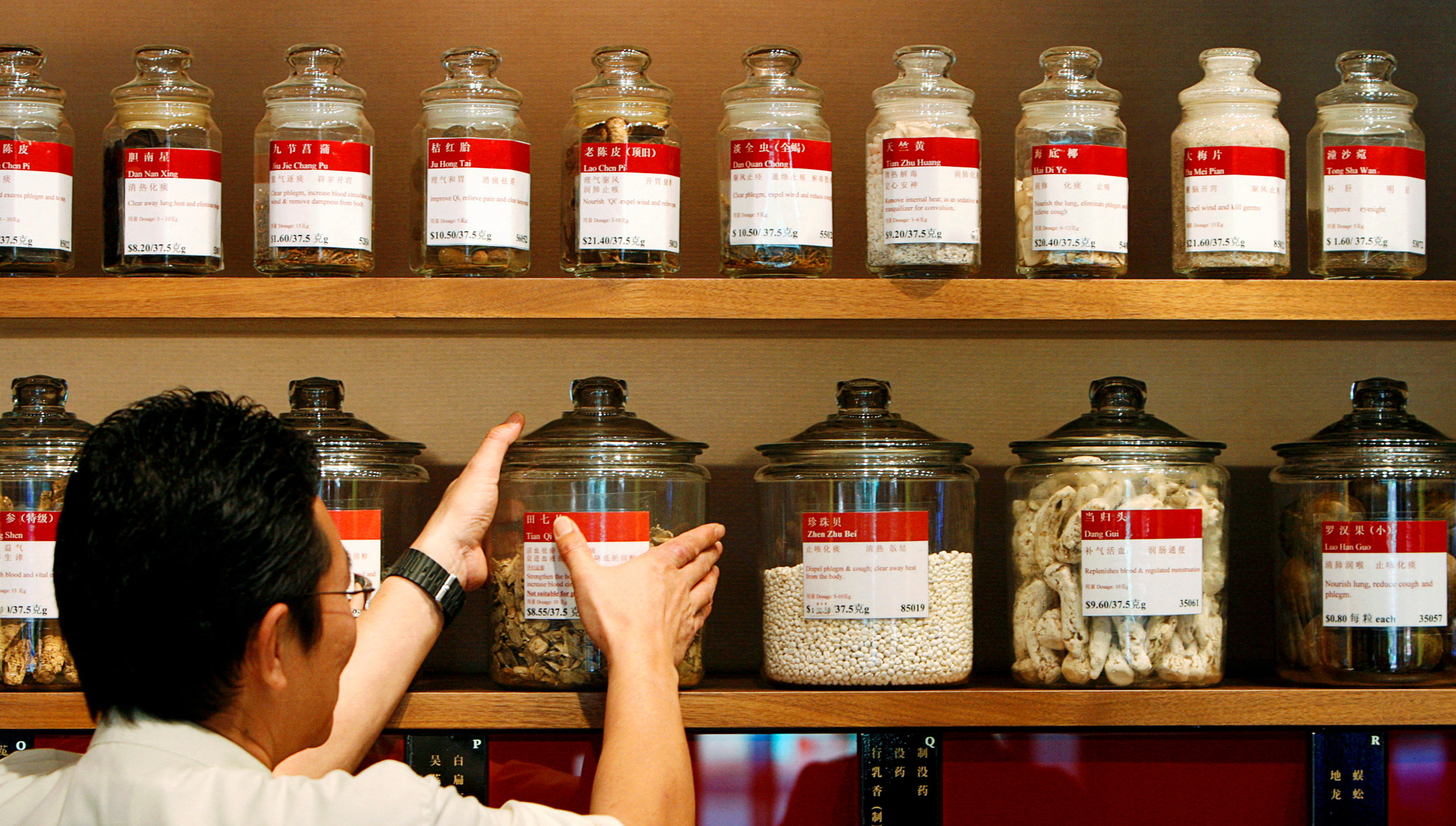 Shop assistant arranges jars containing roots and herbs at Chinese medicine shop in Singapore