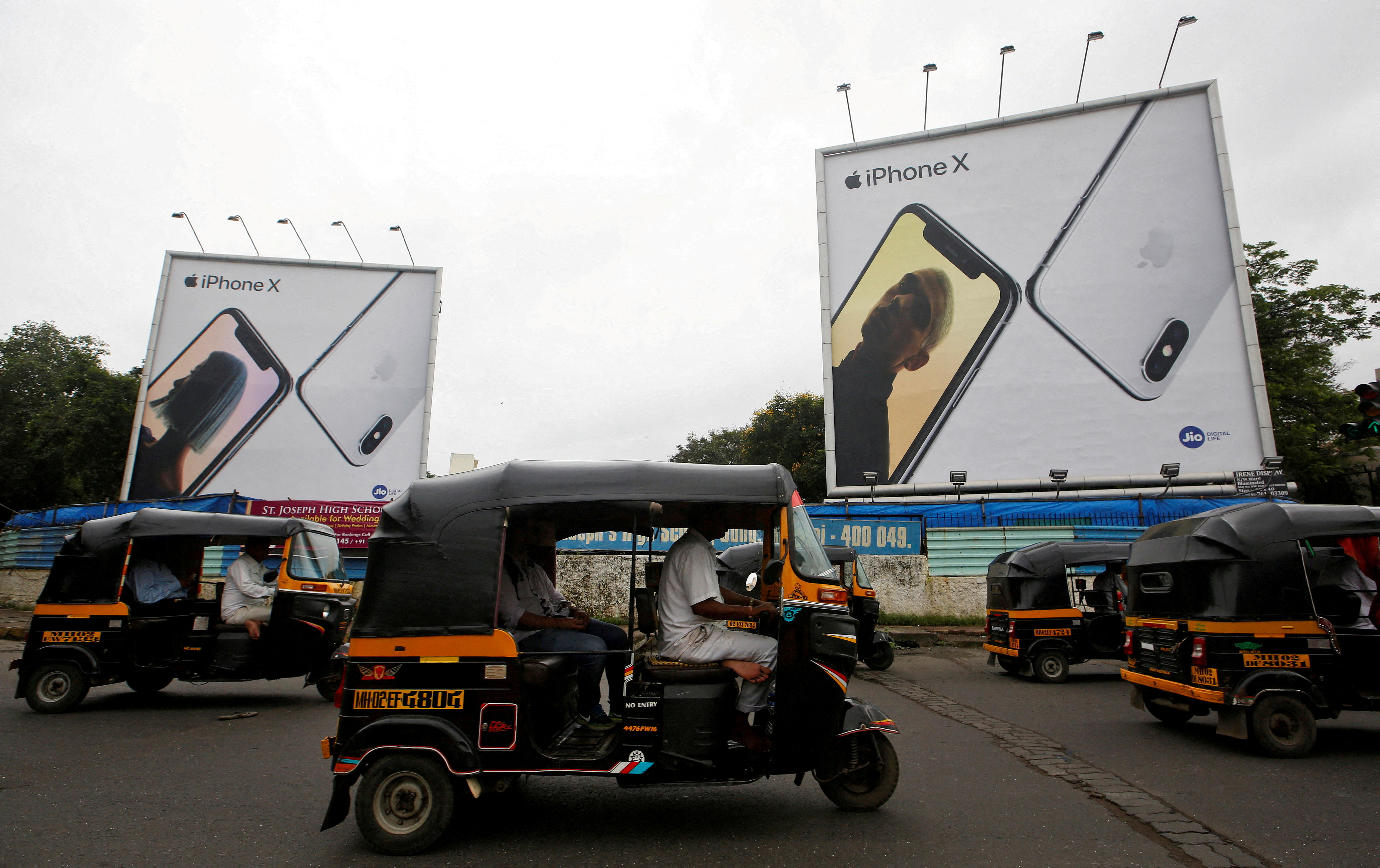 Auto-rickshaws drive past the hoardings of Apple iPhone X mobile phones in Mumbai