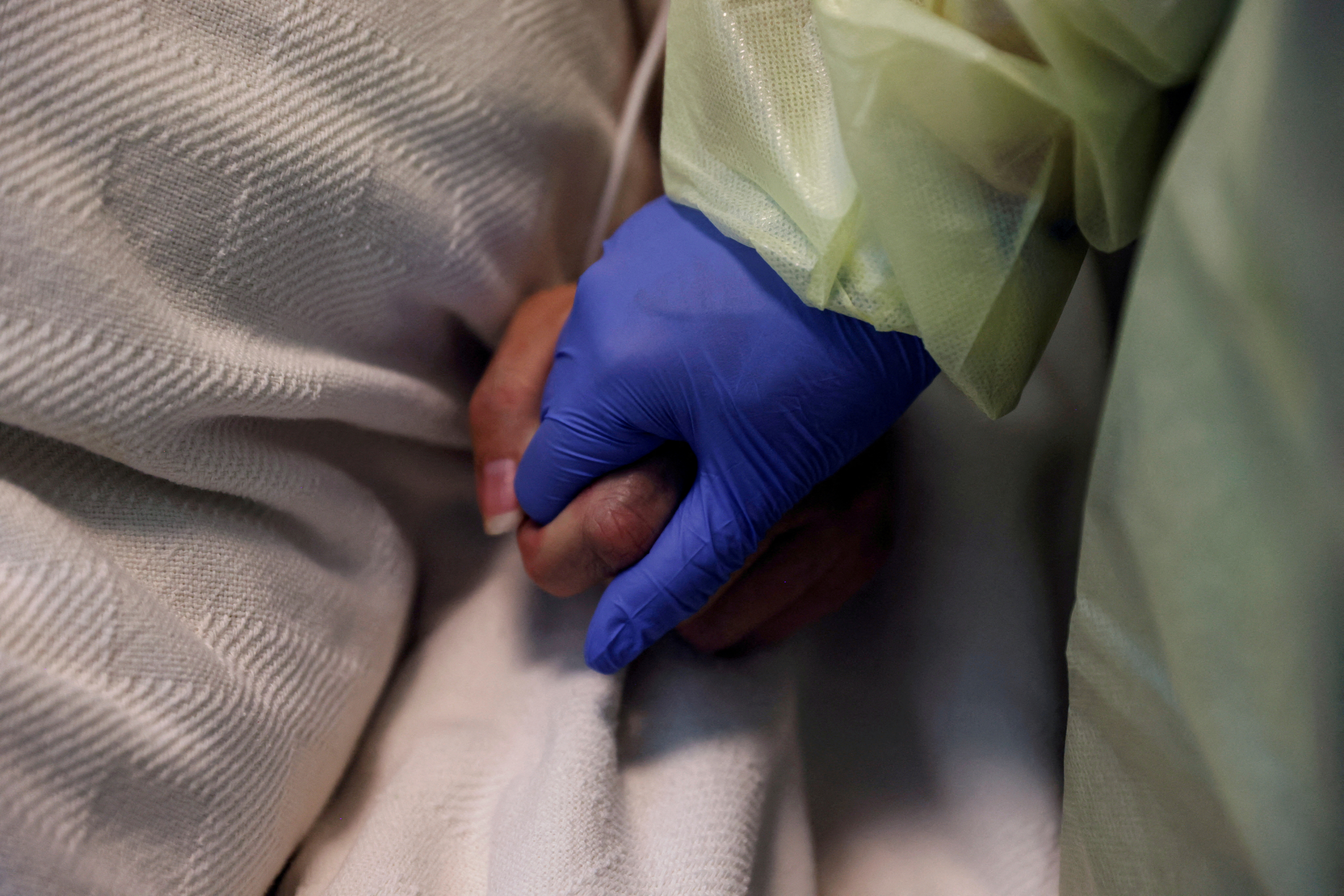 A woman in her personal protective equipment (PPE) gear holds the hand of a coronavirus disease (COVID-19) positive patient, in her isolation room at Madison Memorial Hospital in Rexburg, Idaho, U.S., October 28, 2021. REUTERS/Shannon Stapleton
