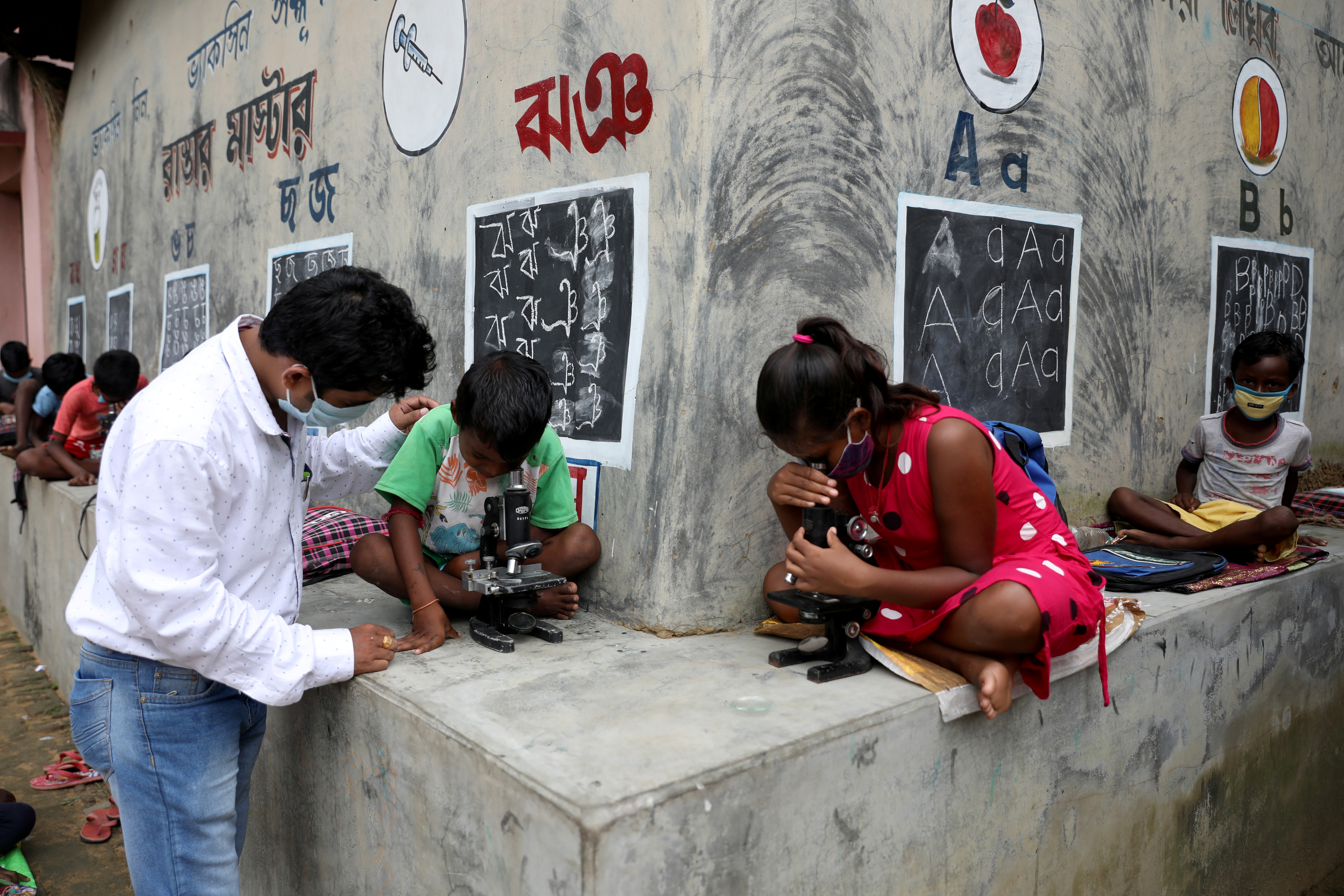 Deep Narayan Nayak teaches children how to use microscope in an open-air class outside the houses with the walls converted into black boards at Joba Attpara village