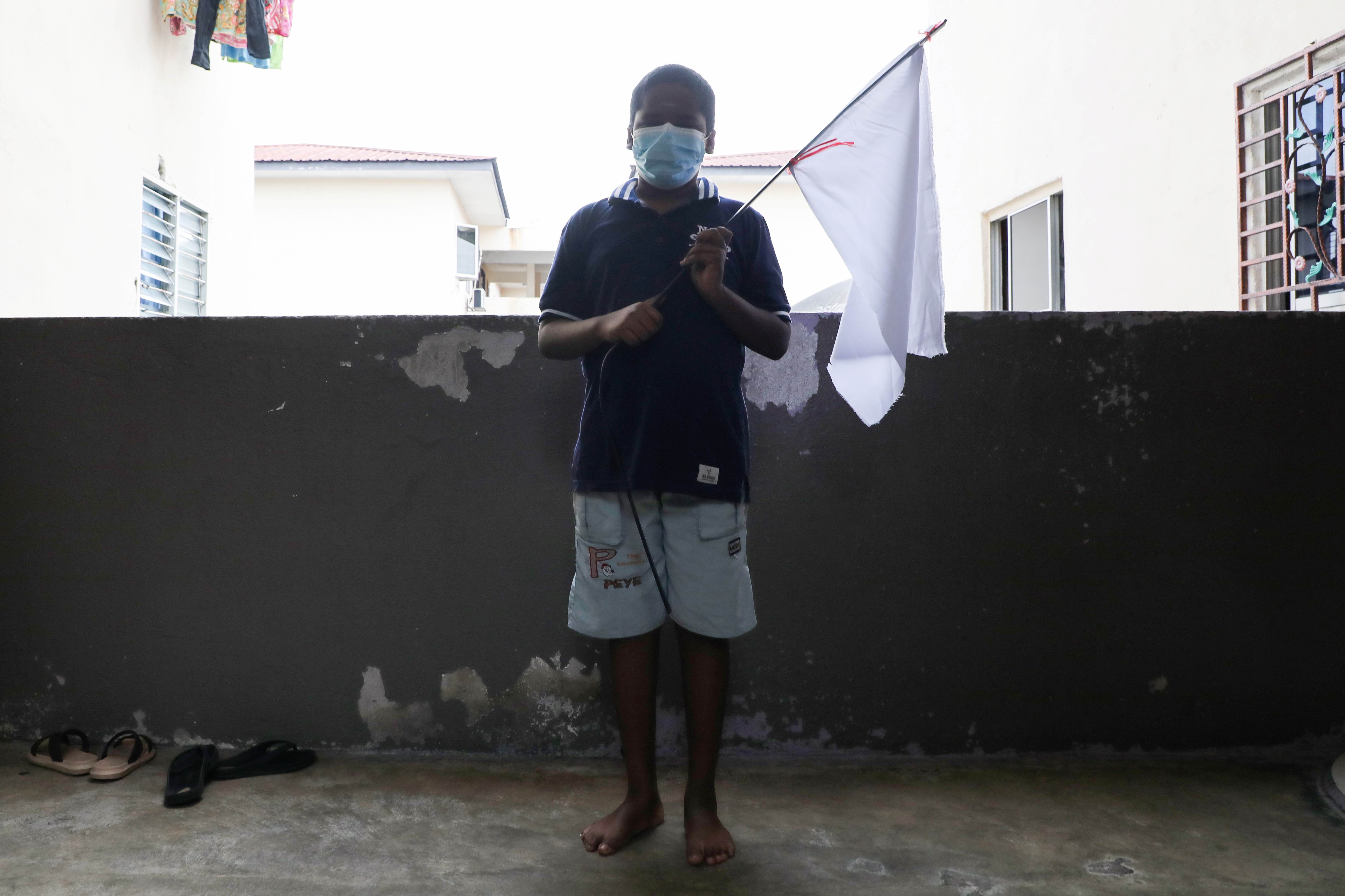 A boy holds a white flag which his family hung to ask for help, during an enhanced lockdown in Petaling Jaya