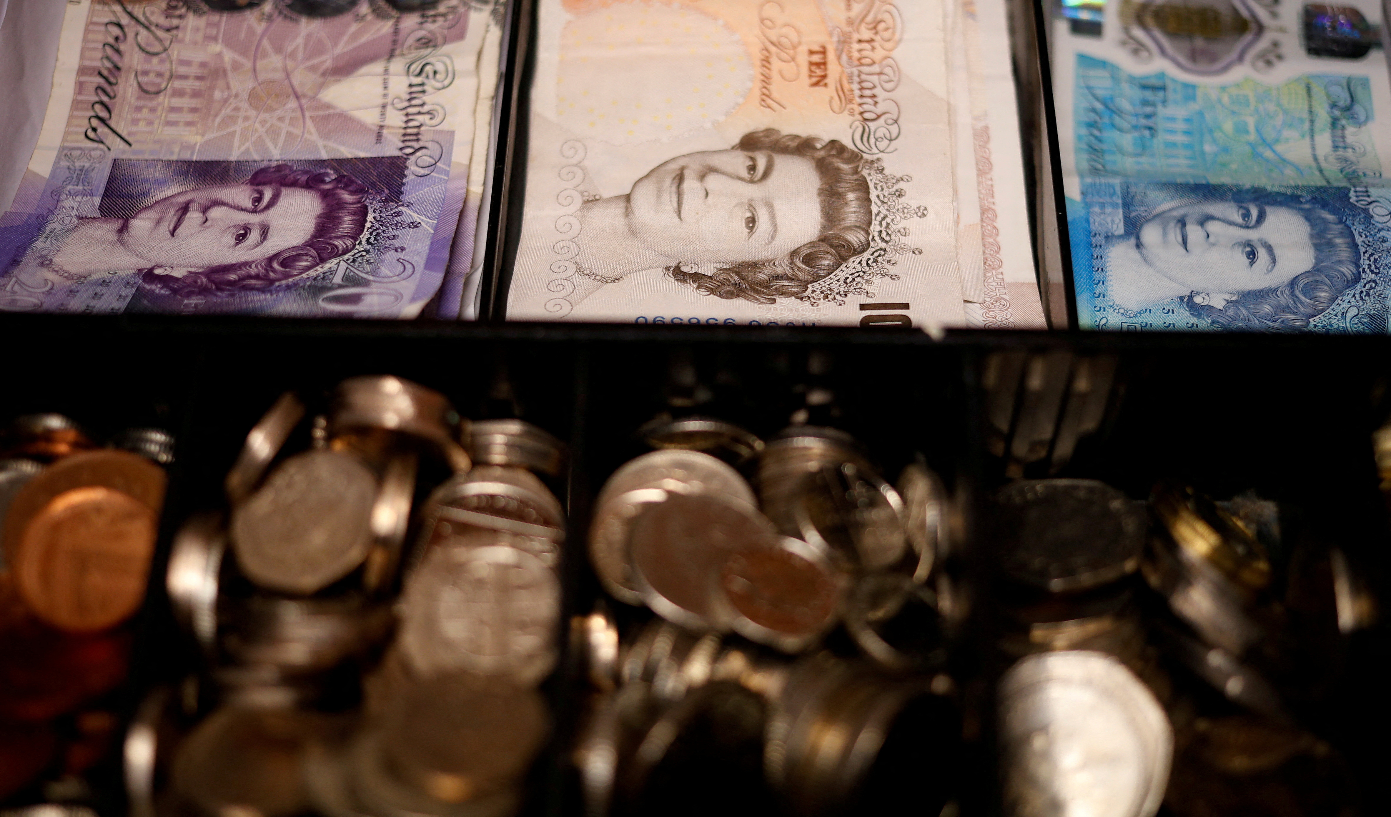 Pound notes and coins are seen inside a cash register in a bar in Manchester, Britain