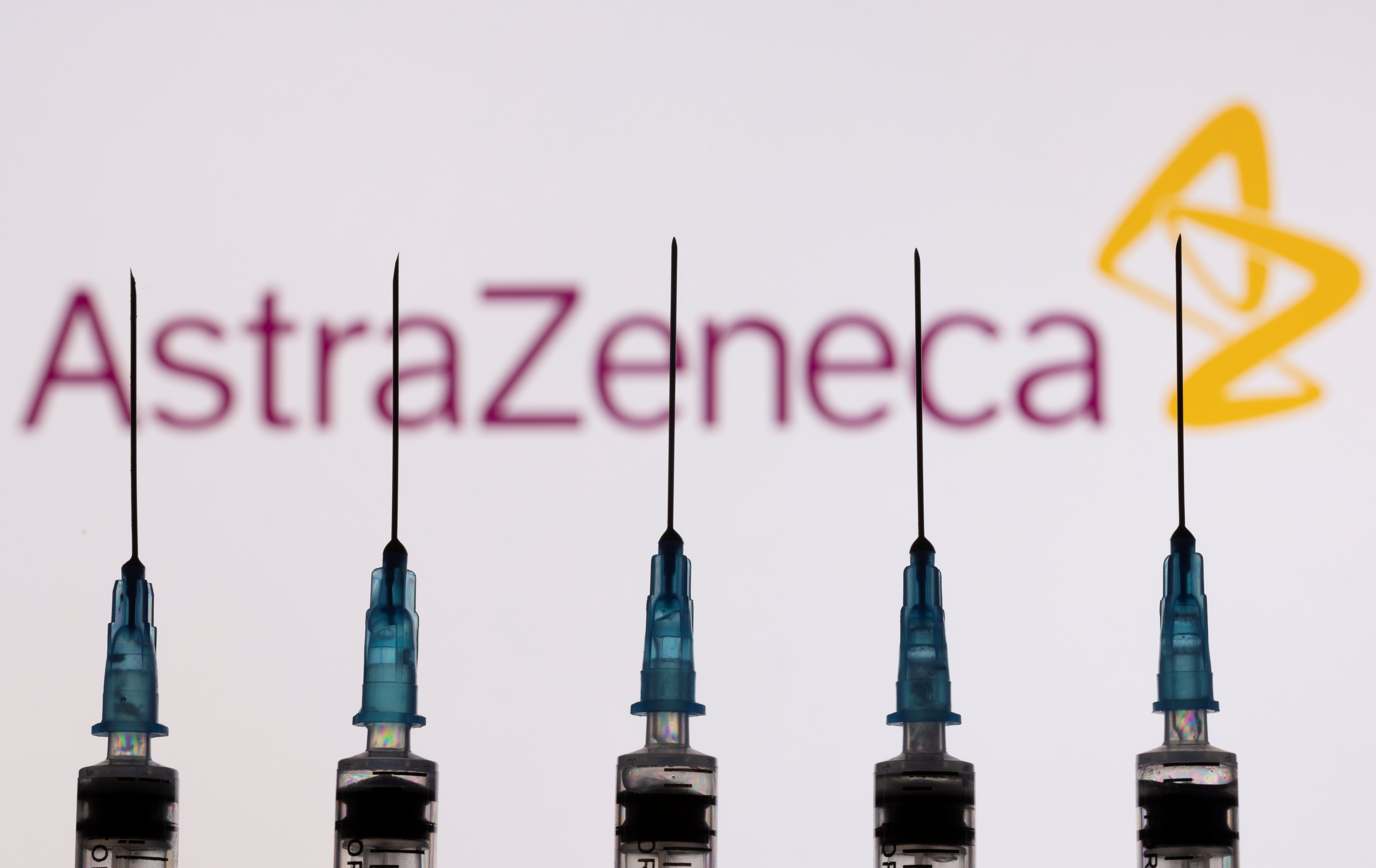 Syringes with needles are seen in front of a displayed AstraZeneca logo in this illustration taken