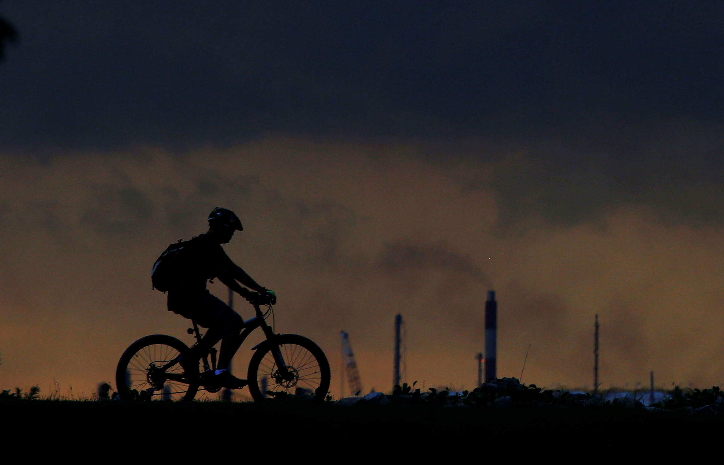 A man cycles past a chimney giving off emissions in an industrial area of Singapore