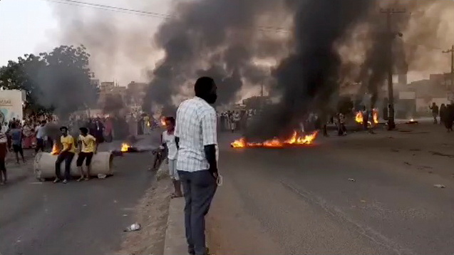 People gather as fire and smoke are seen on the streets of Kartoum, Sudan, amid reports of a coup