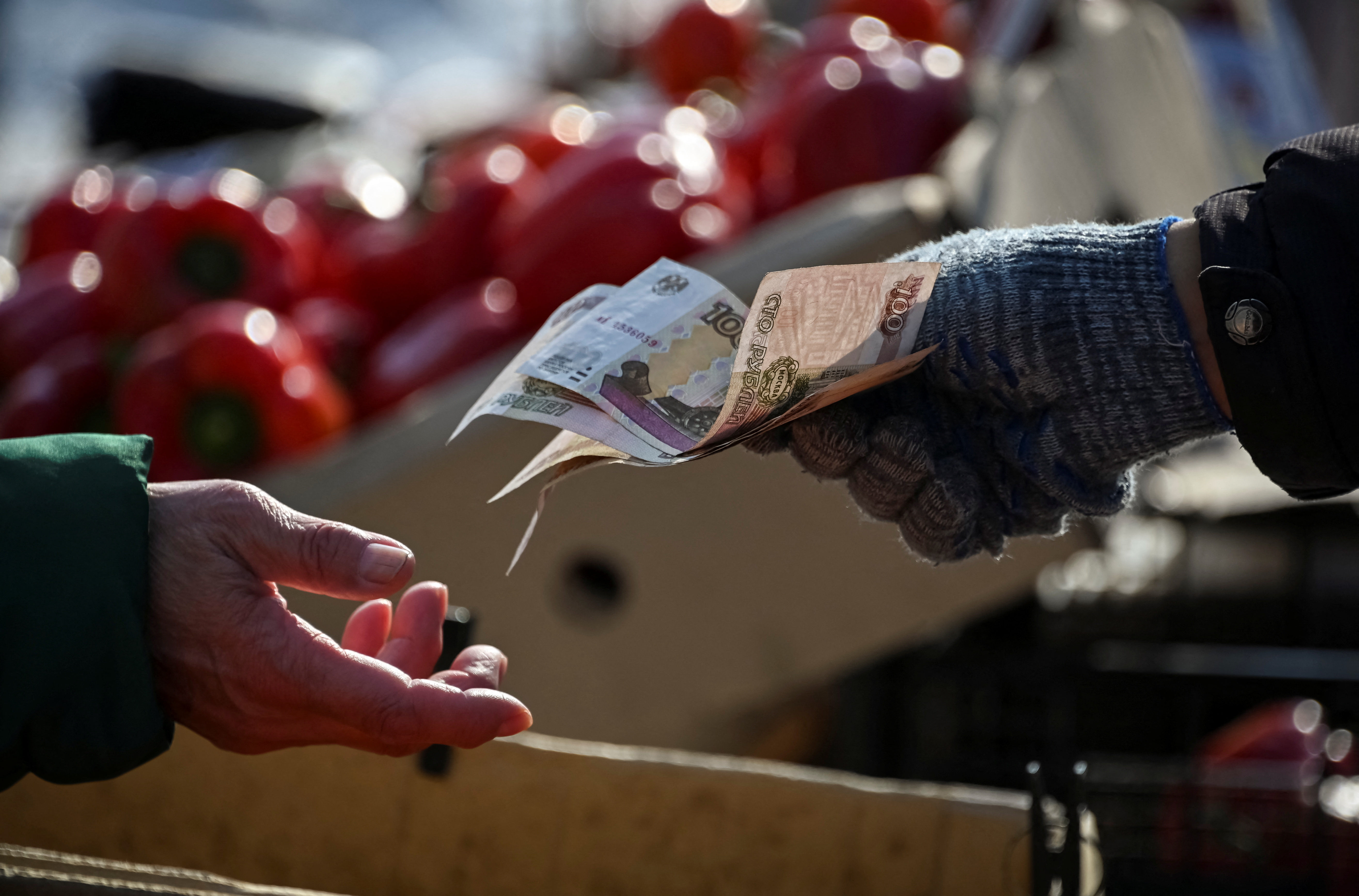 A vendor hands over Russian rouble banknotes to a customer at a street market in Omsk