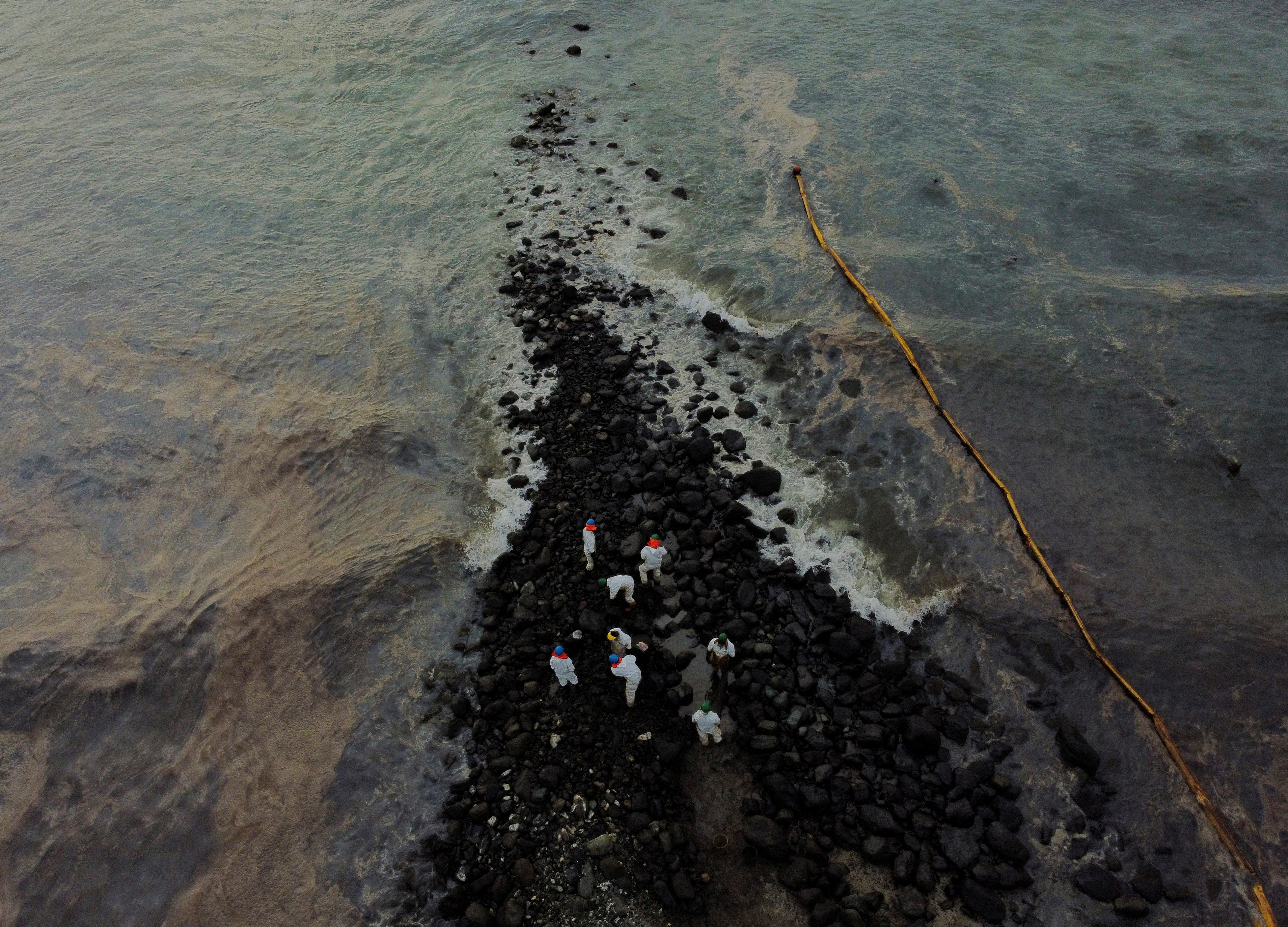 Workers clean the beach near Repsol's La Pampilla refinery after recent oil spill, in Ventanilla