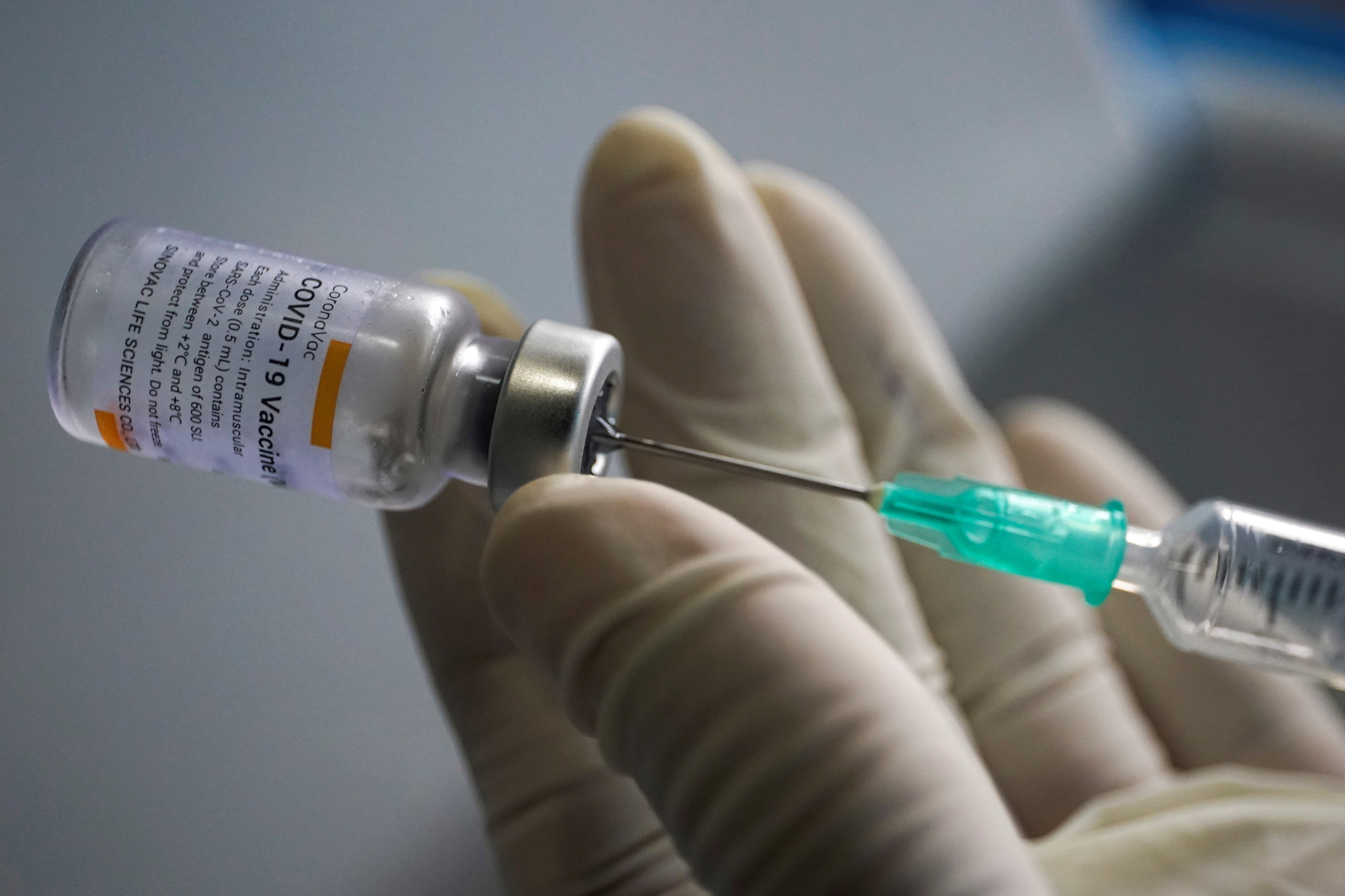 A health worker holds a syringe and a vial of the Sinovac coronavirus disease (COVID-19) vaccine at a market in Bangkok