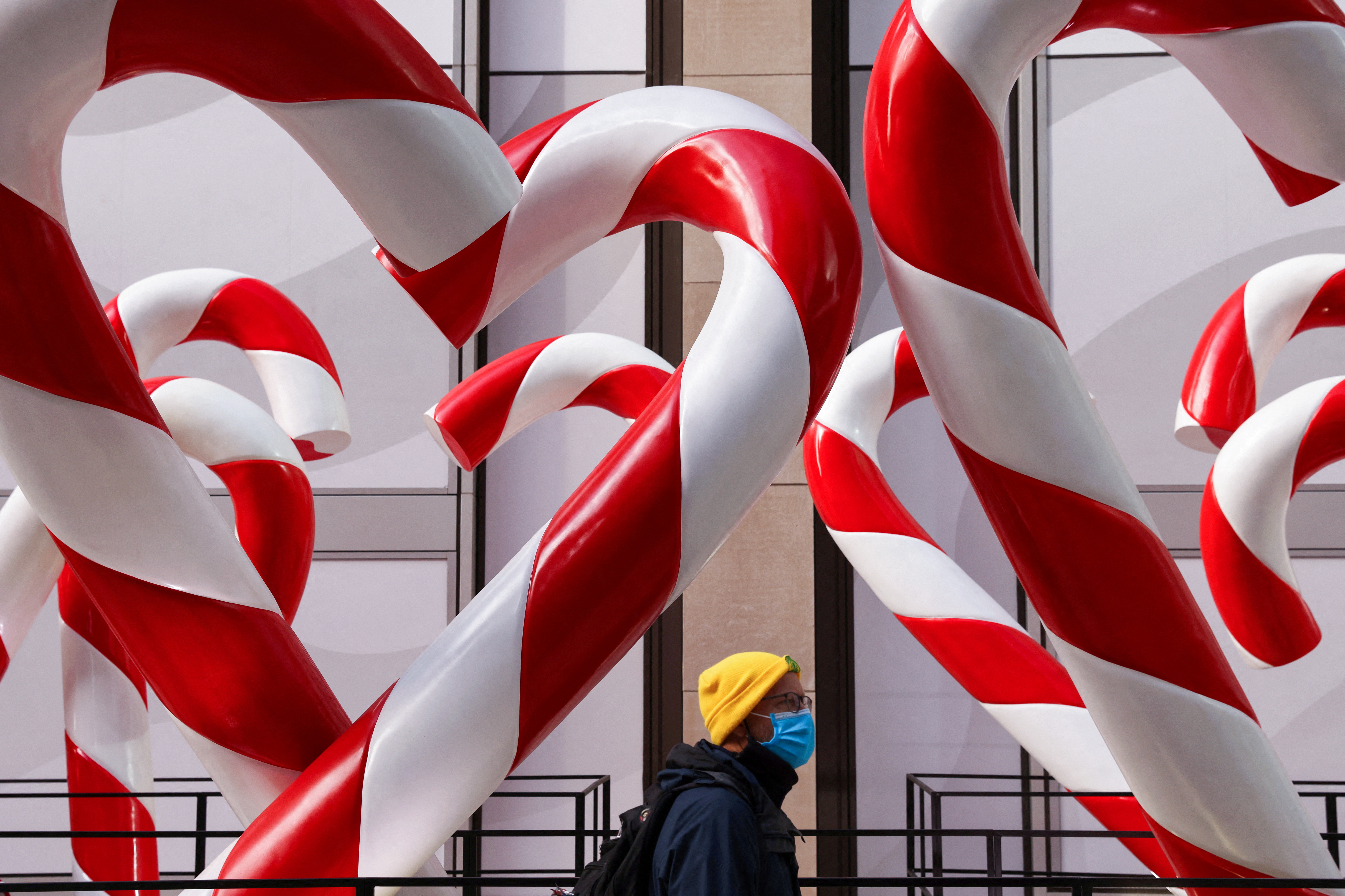 A person in a face mask walks by holiday decorations on Sixth Avenue as the Omicron coronavirus variant continues to spread in Manhattan, New York City