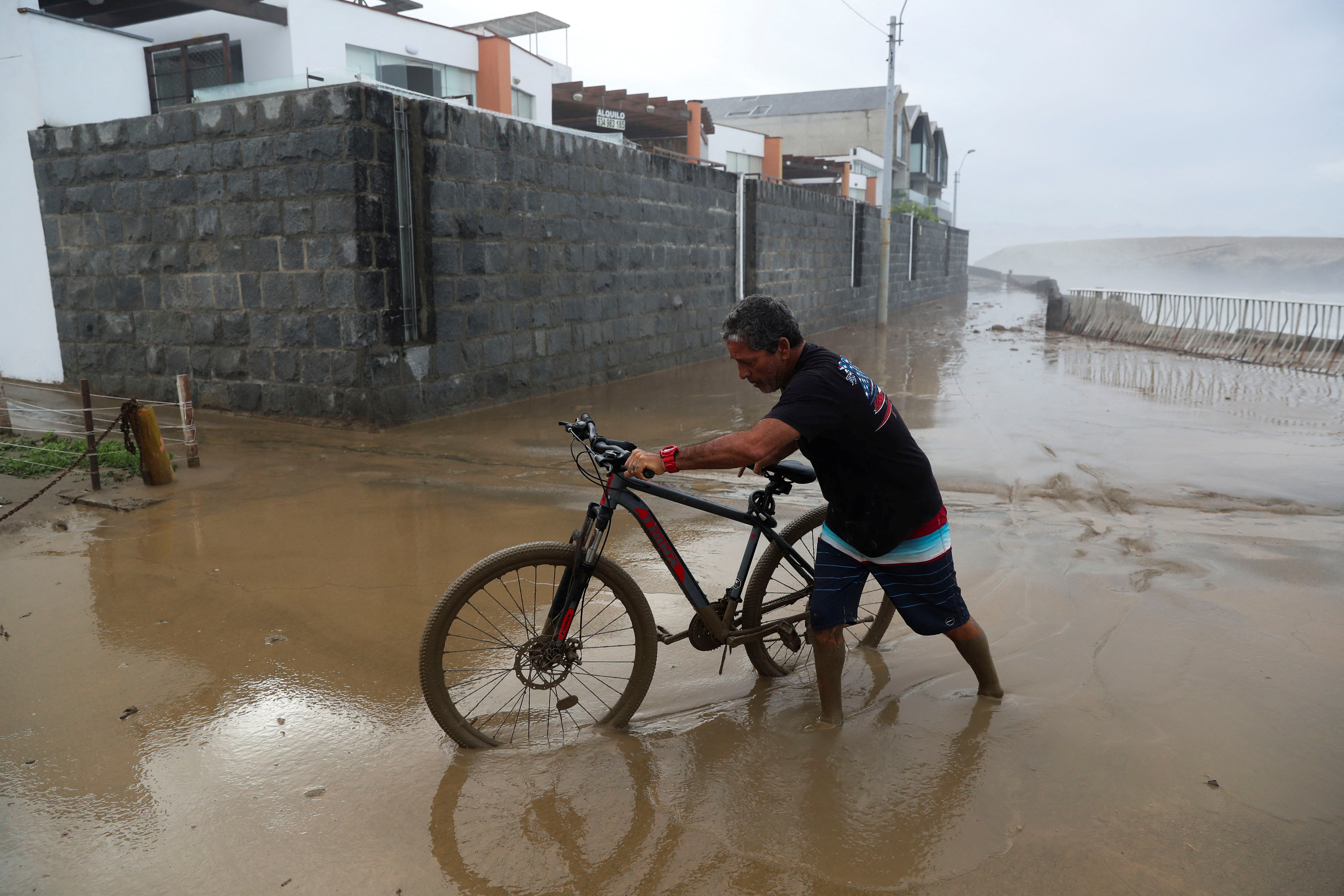 A man carries moves his bicycle in a flooded street following Cyclone Yaku in Lima