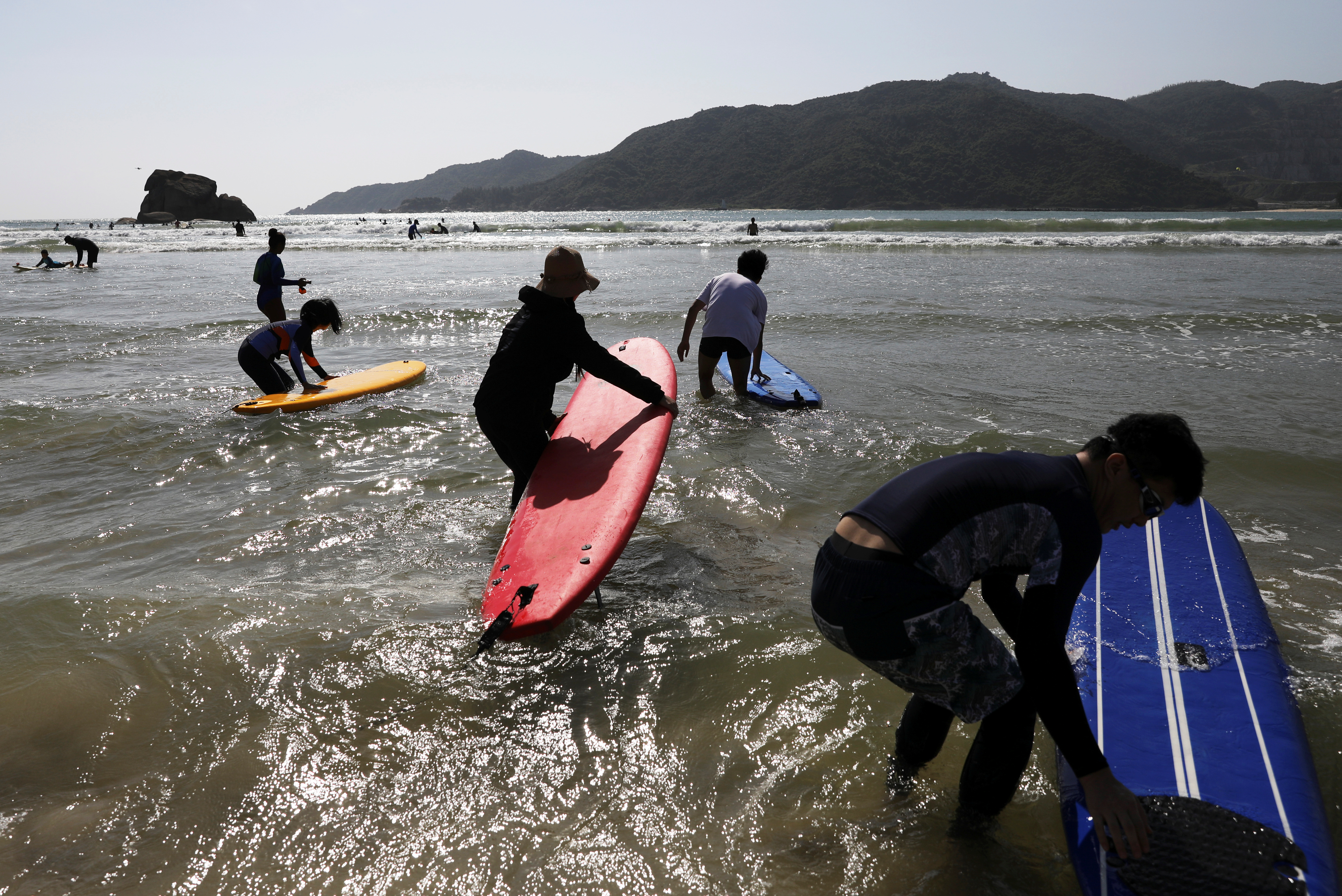 Surfers push their surfing boards as they head into the sea in Sanya
