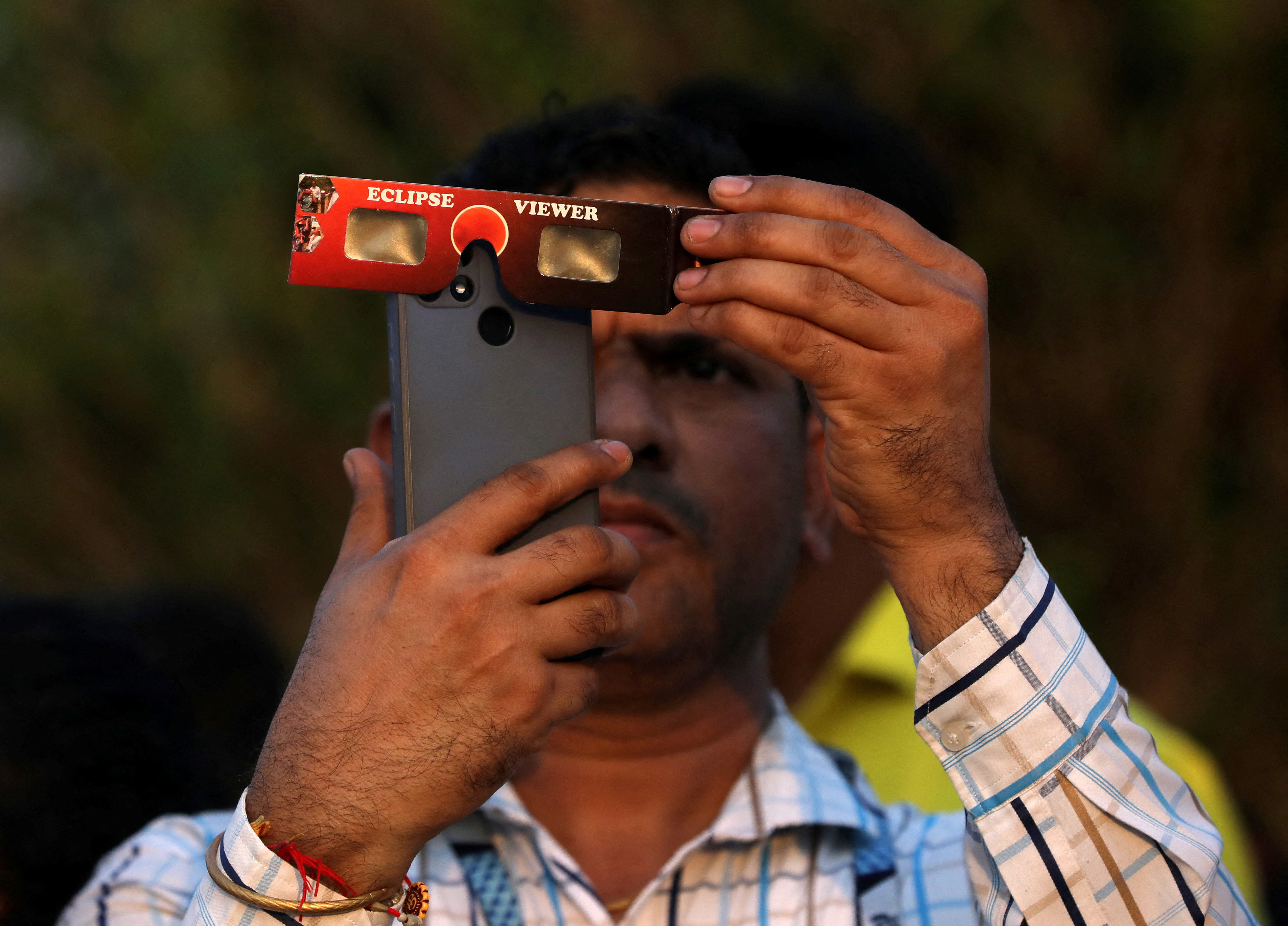 A man uses solar viewers to record a partial solar eclipse on his mobile phone in Mumbai