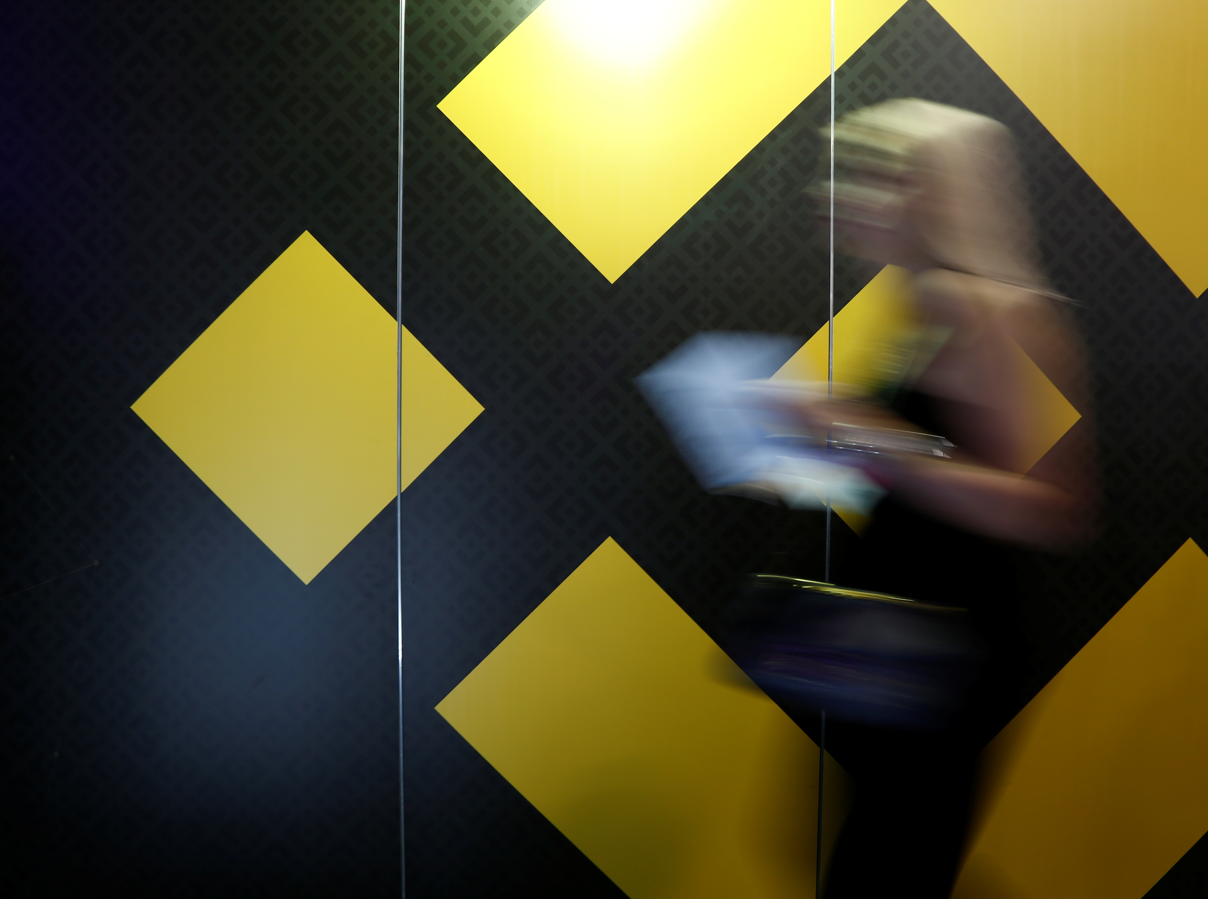 A woman walks past an exhibition stand showing the logo of Binance at the Delta Summit in St Julian's