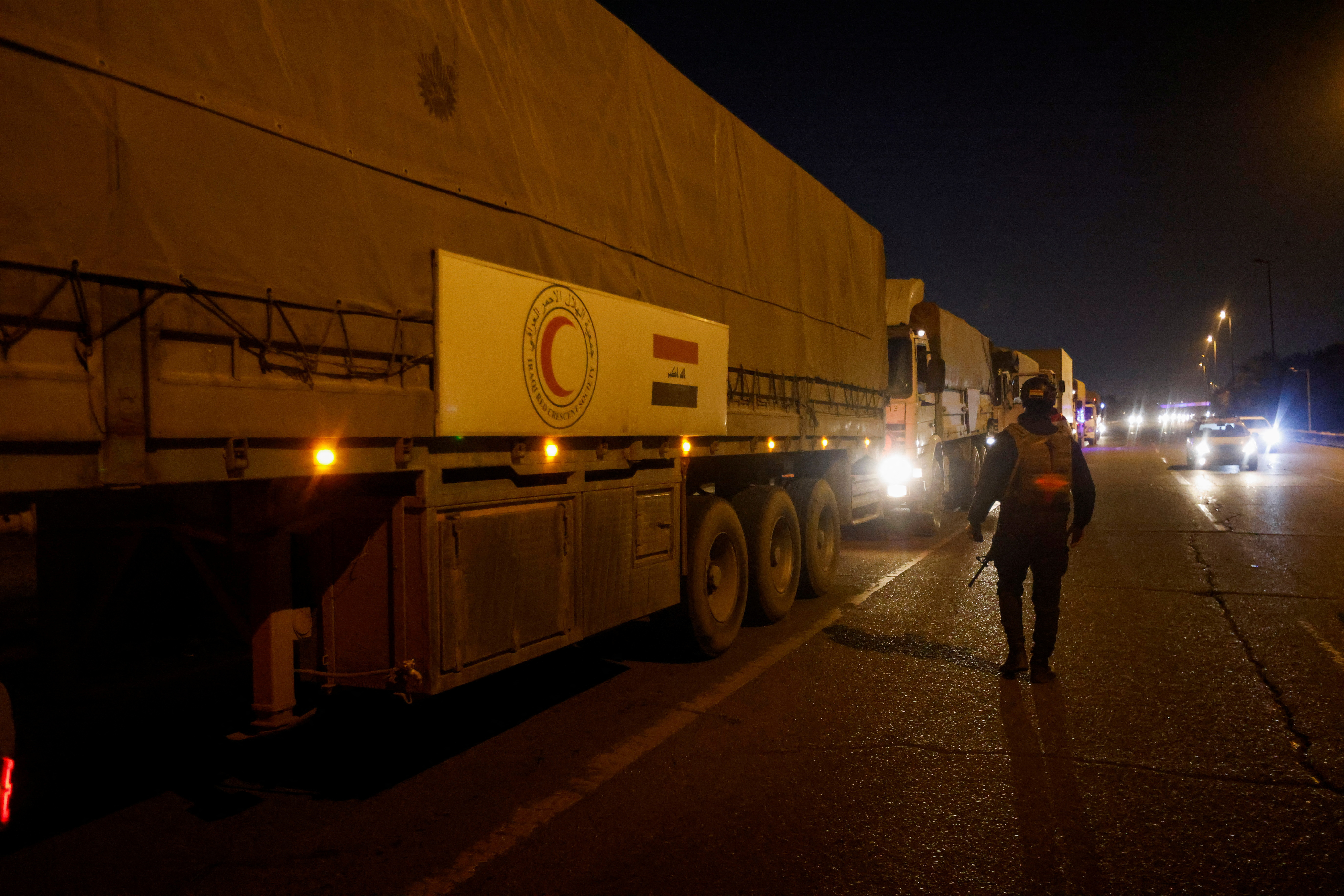 A member of Iraqi security forces walks past Red Crescent vehicles that are carrying aids heading to a plane of emergency relief aid to Syria, in Baghdad
