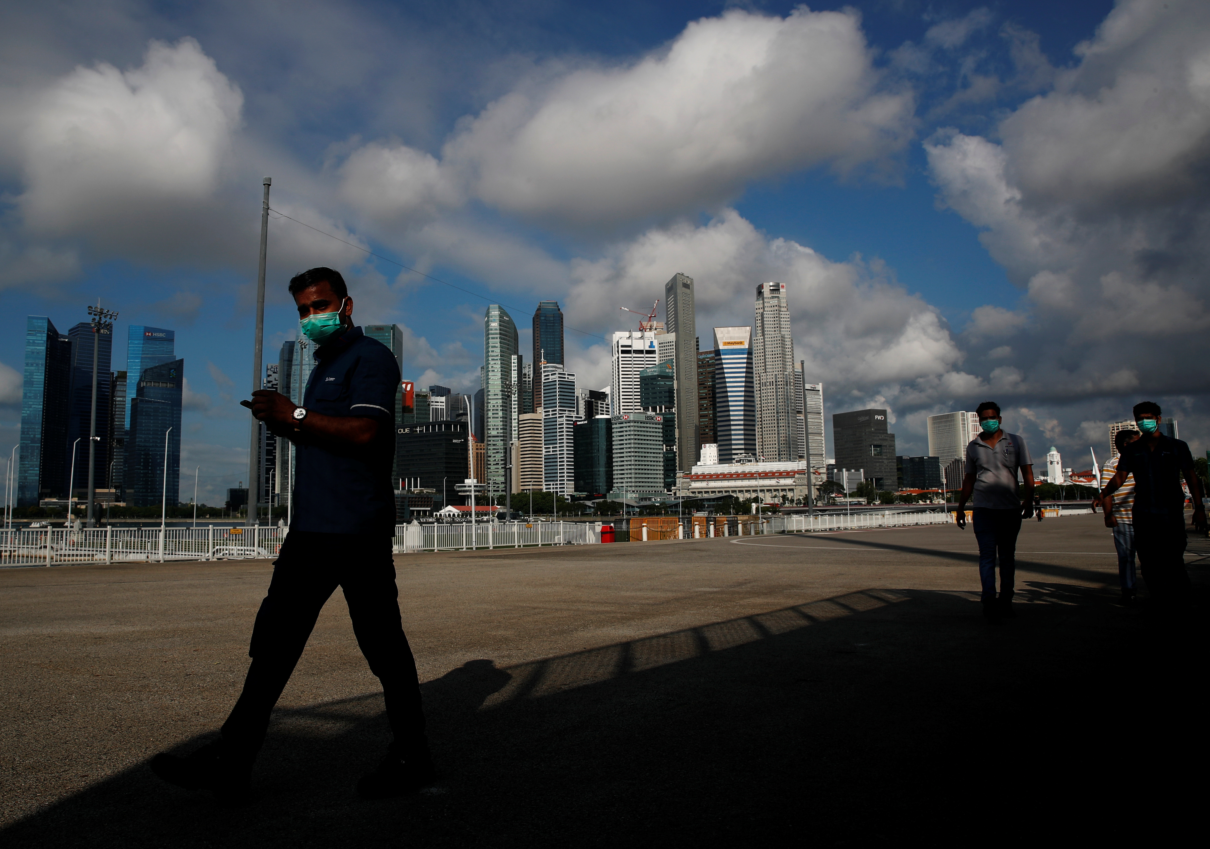 Essential workers wearing face masks walk past the skyline of the central business district outside a regional screening center amid the coronavirus disease (COVID-19) outbreak in Singapore June 9, 2020.  REUTERS/Edgar Su/Files