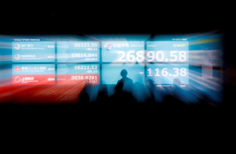 Silhouettes of passerby are seen as they stand in front of an electric monitor displaying Japan's Nikkei share average and world stock indexes in Tokyo