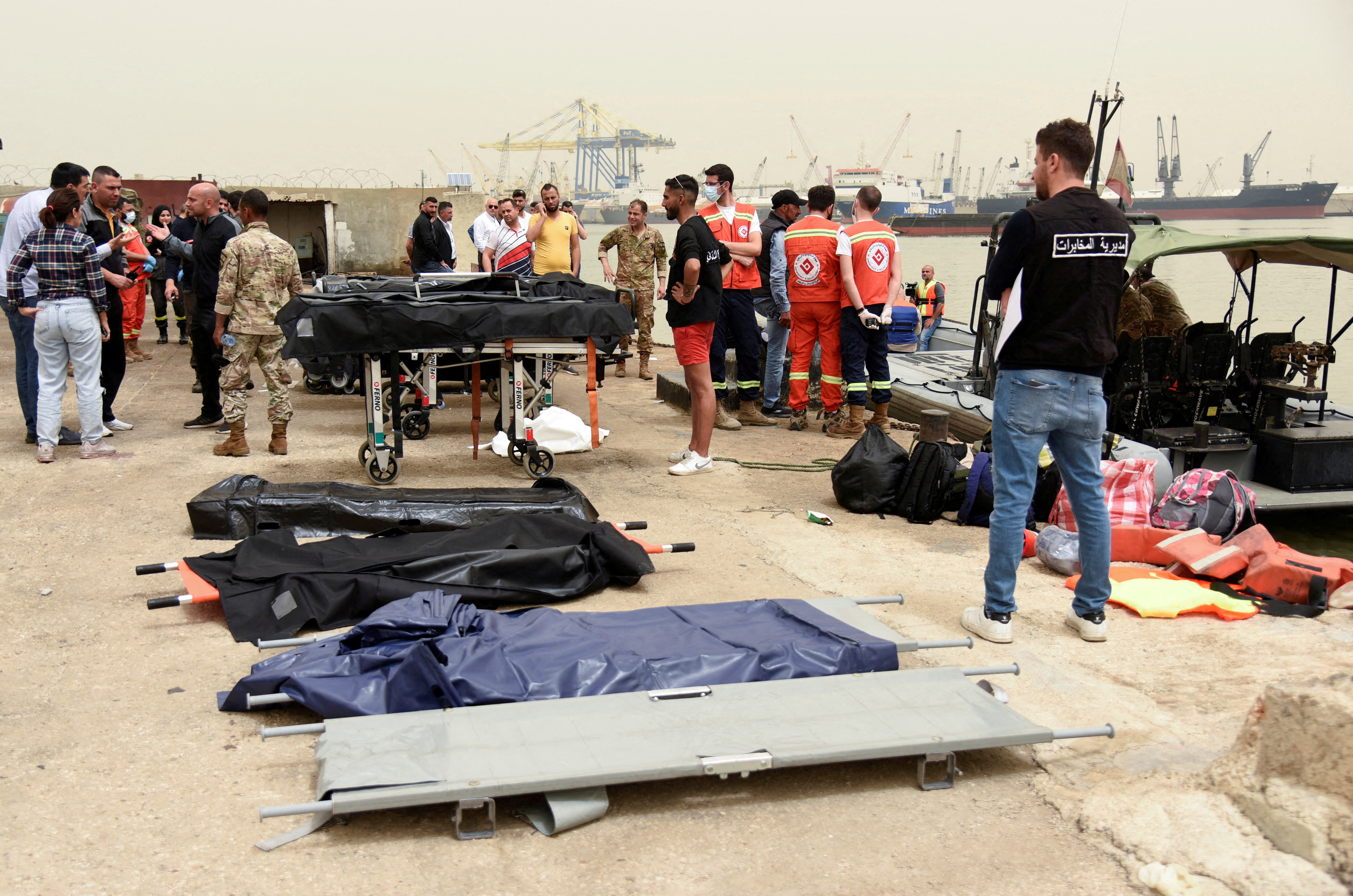 People stand near stretchers after a boat capsized off the Lebanese coast of Tripoli overnight, at port of Tripoli