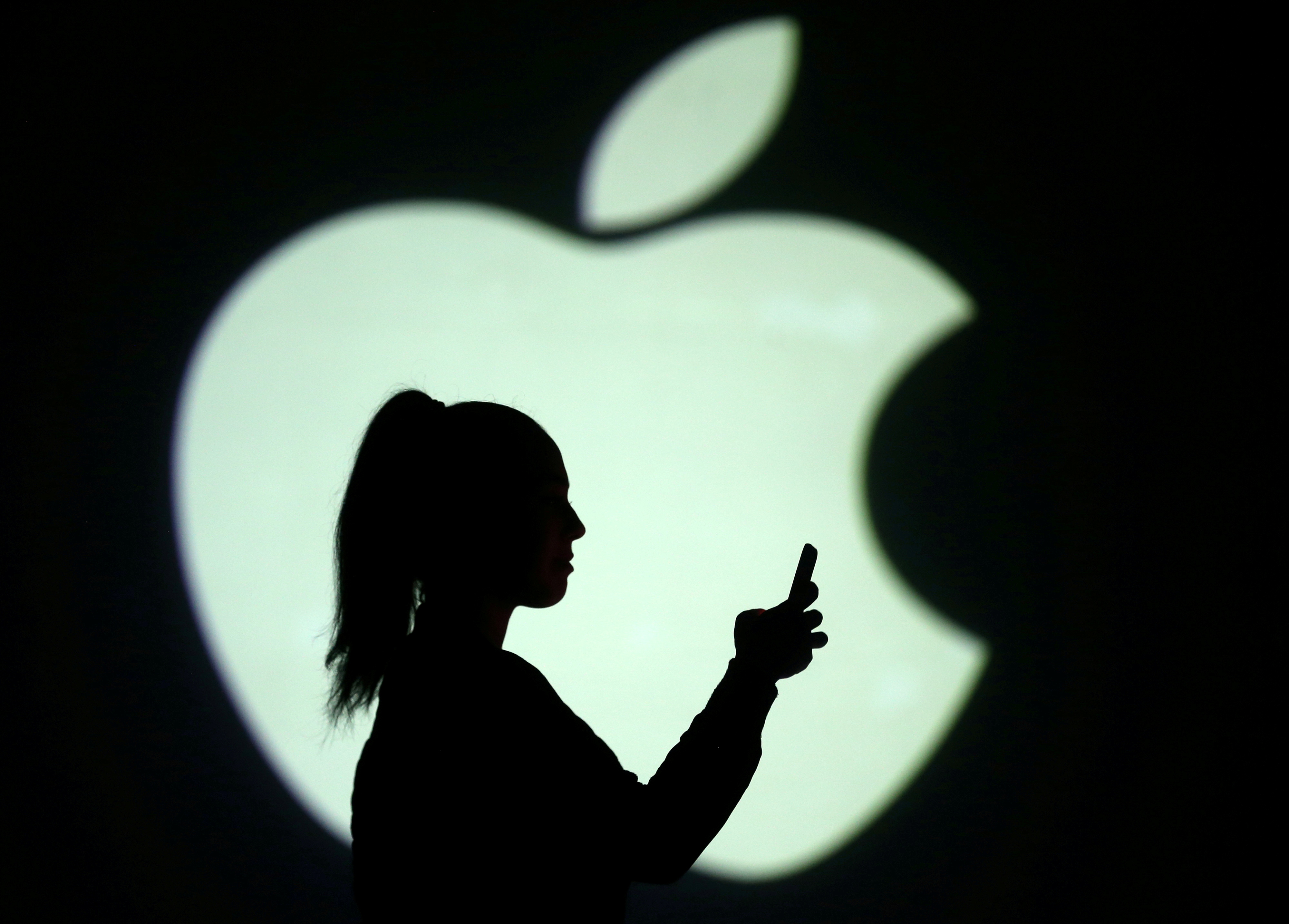 Silhouette of a mobile user seen next to a screen projection of the Apple logo in this picture illustration taken March 28, 2018.  REUTERS/Dado Ruvic/Illustration/File Photo