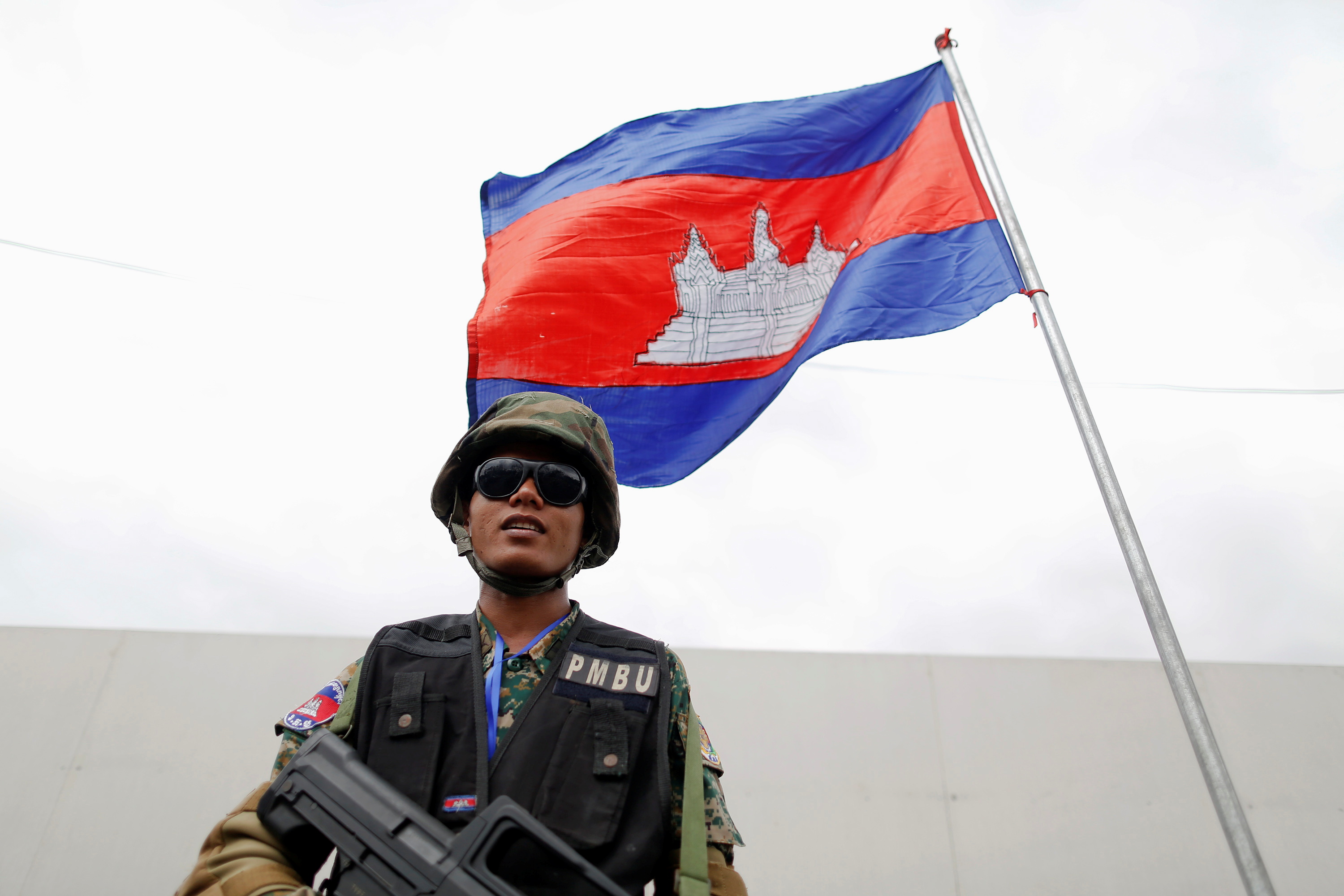 An armed security guard stands under a Cambodian flag in Phnom Penh