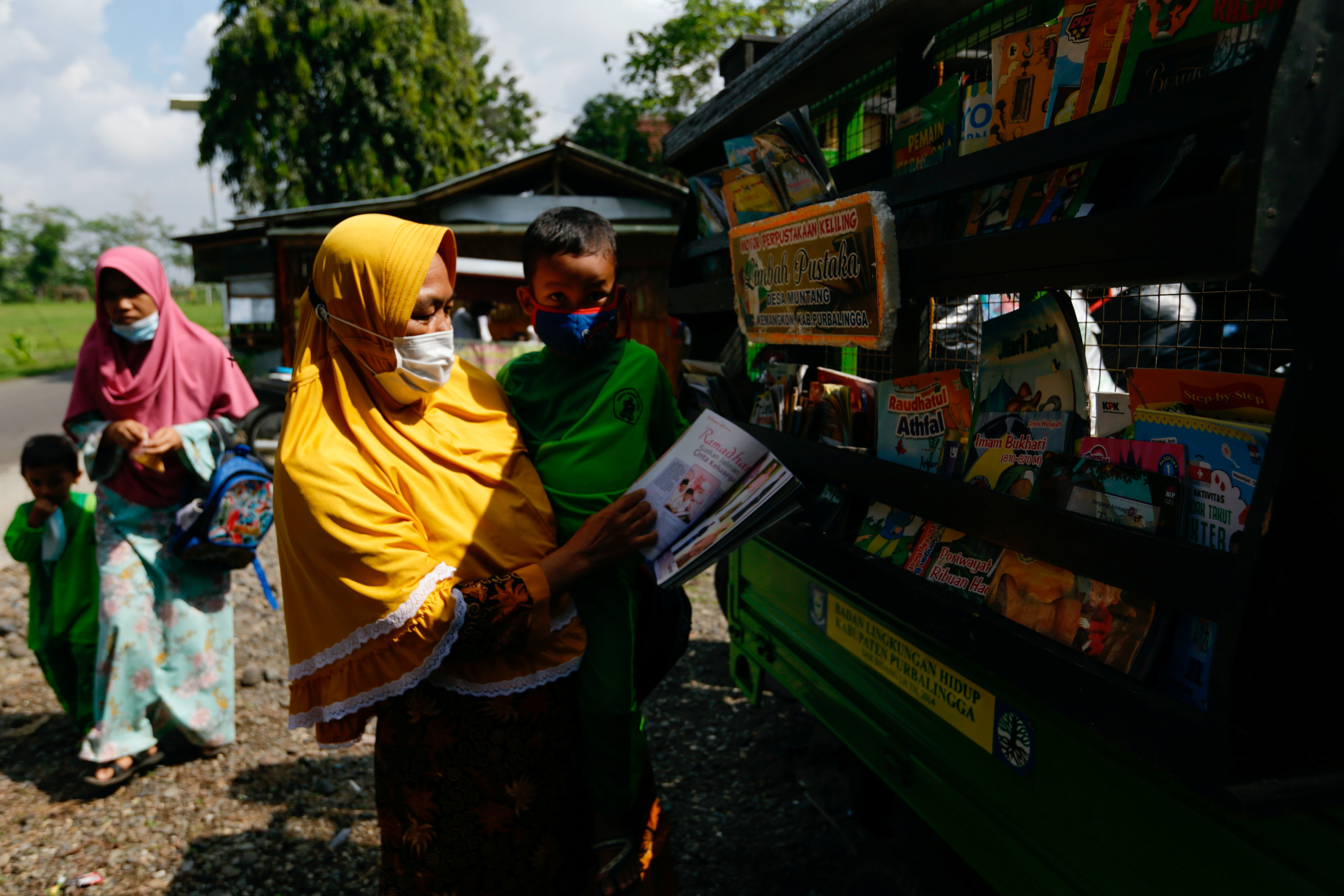 A woman carries a boy who chooses a book on the mobile library at a kindergarten in Muntang village, Purbalingga, Central Java province, Indonesia November 2, 2021. REUTERS/Ajeng Dinar Ulfiana