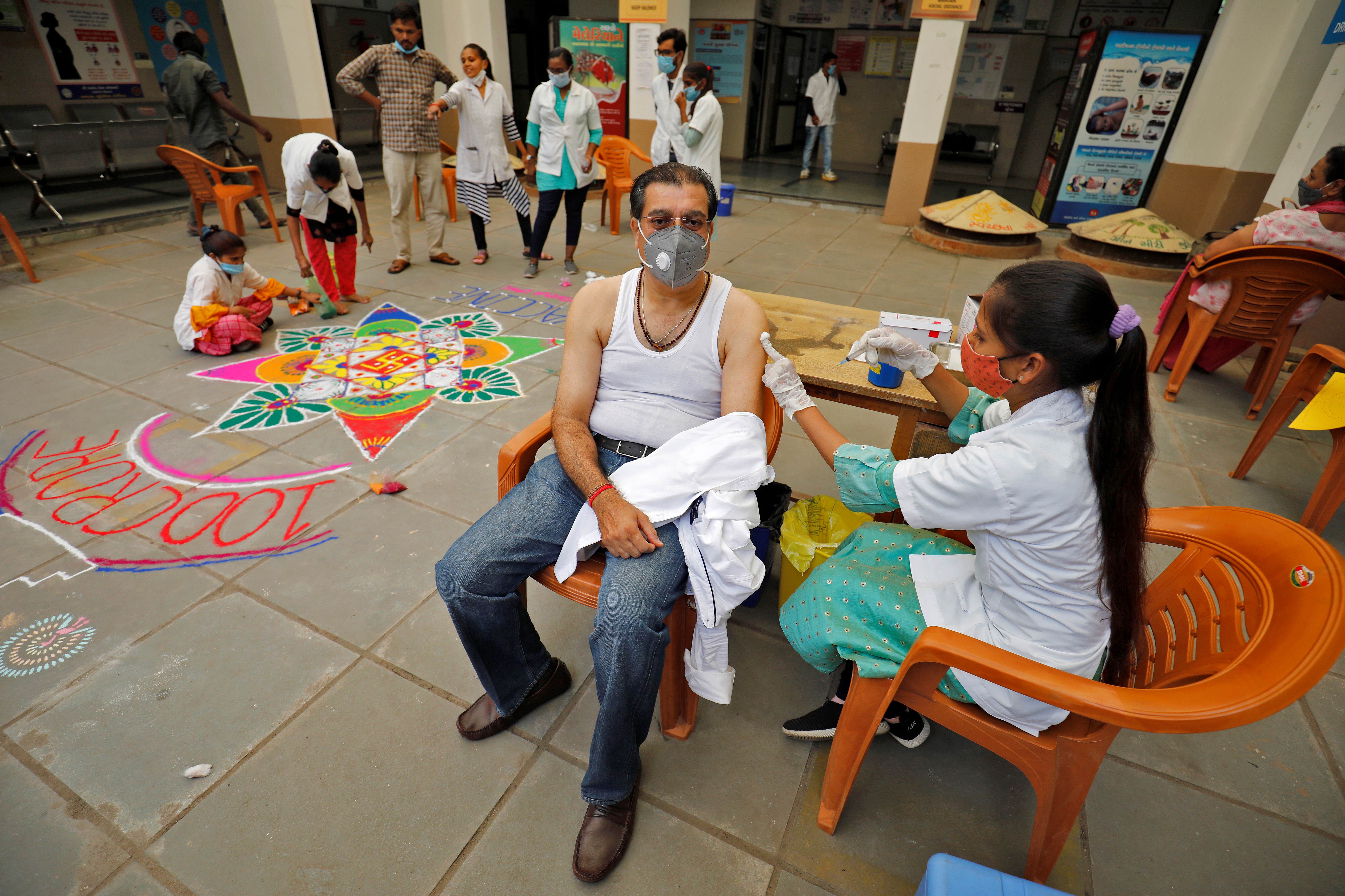 A healthcare worker gives a dose of the COVISHIELD vaccine against the coronavirus disease (COVID-19), manufactured by Serum Institute of India, to a man as others decorate the vaccination centre to celebrate the milestone of administering one billion COVID-19 vaccine doses, in Ahmedabad, India, October 21, 2021. REUTERS/Amit Dave