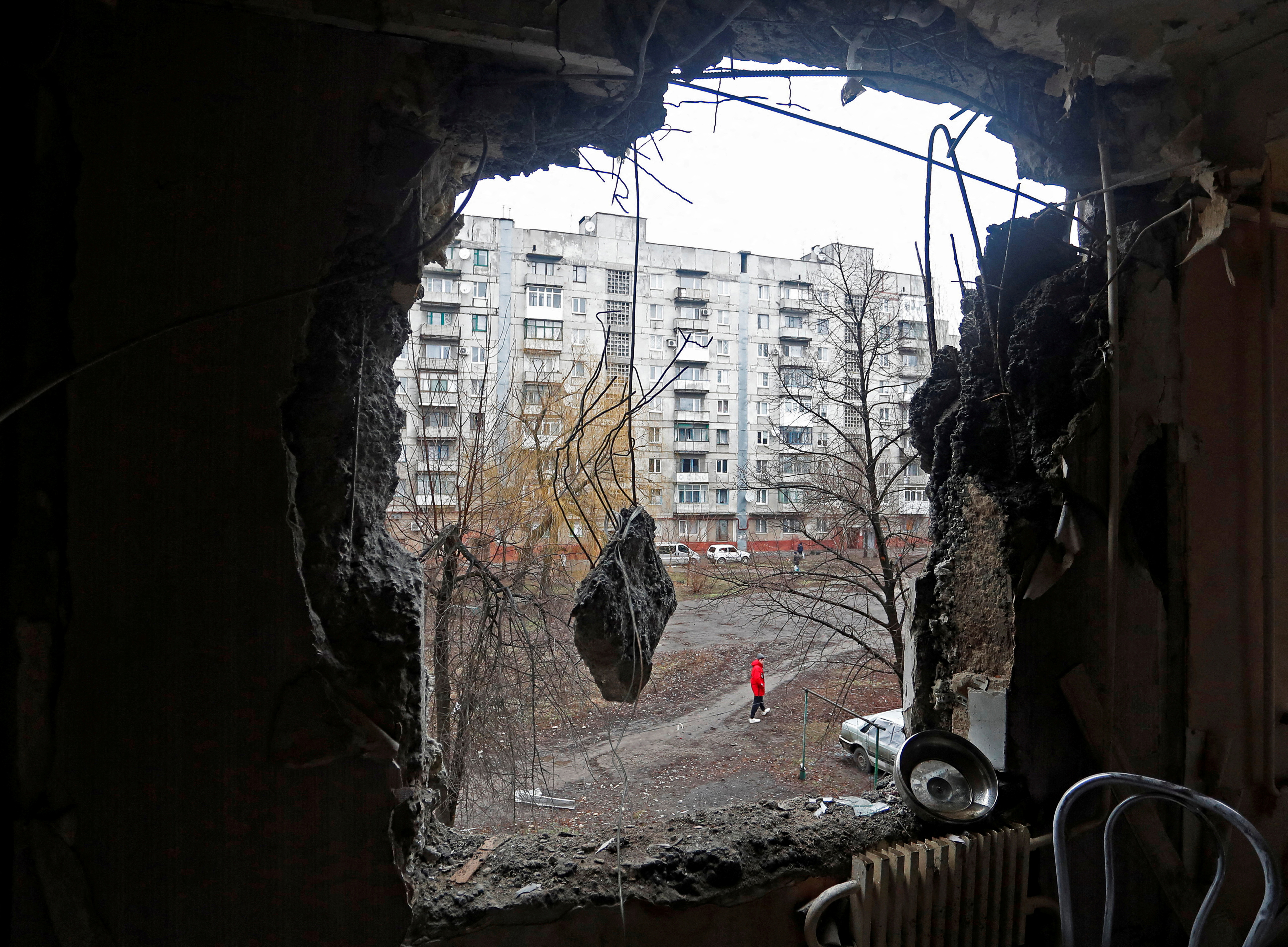 A person walking on the street is pictured through a hole in the wall of a residential building, which locals said was damaged by recent shelling, in Horlivka
