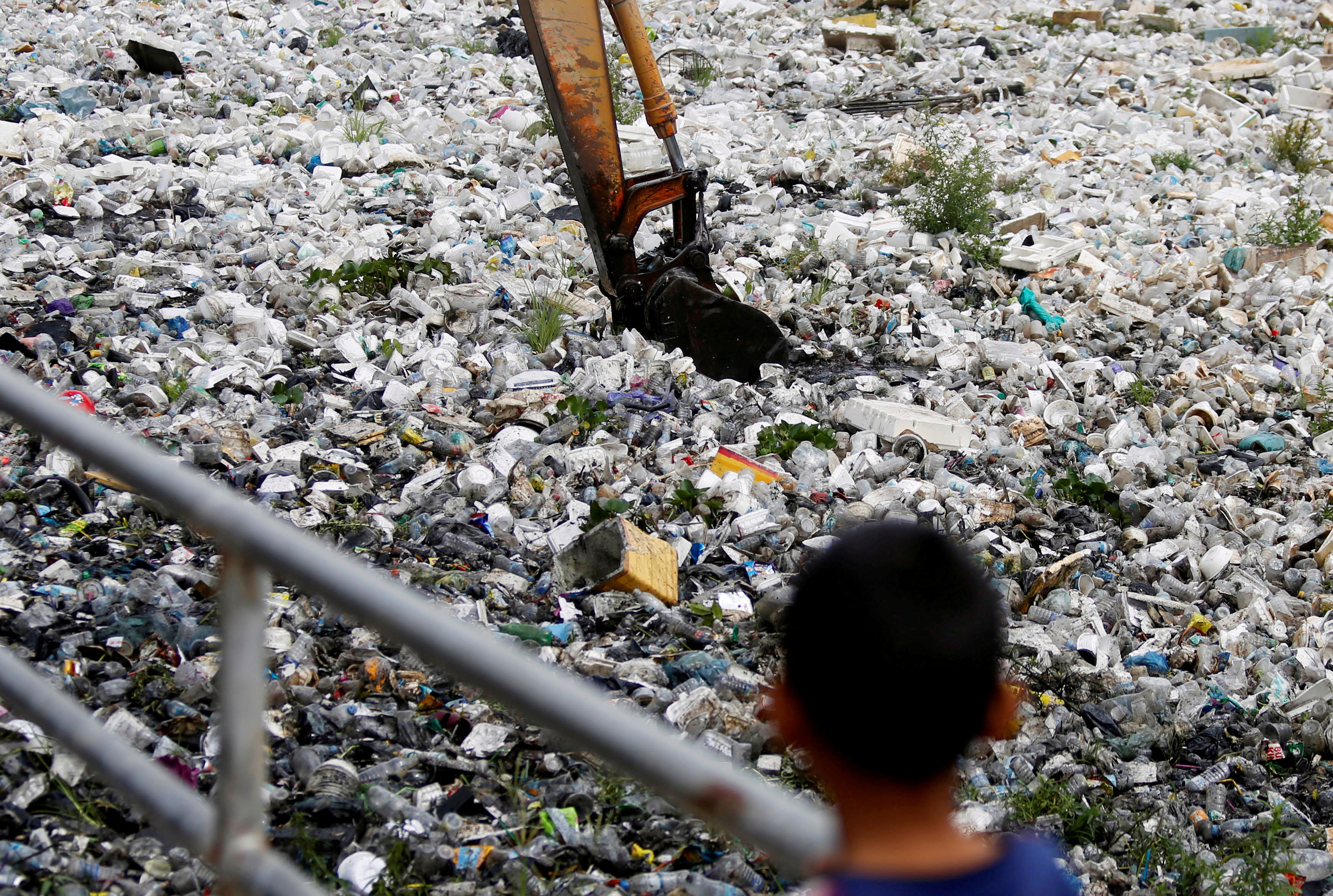A child watches as heavy machinery collects rubbish at a sewage canal in Phnom Penh