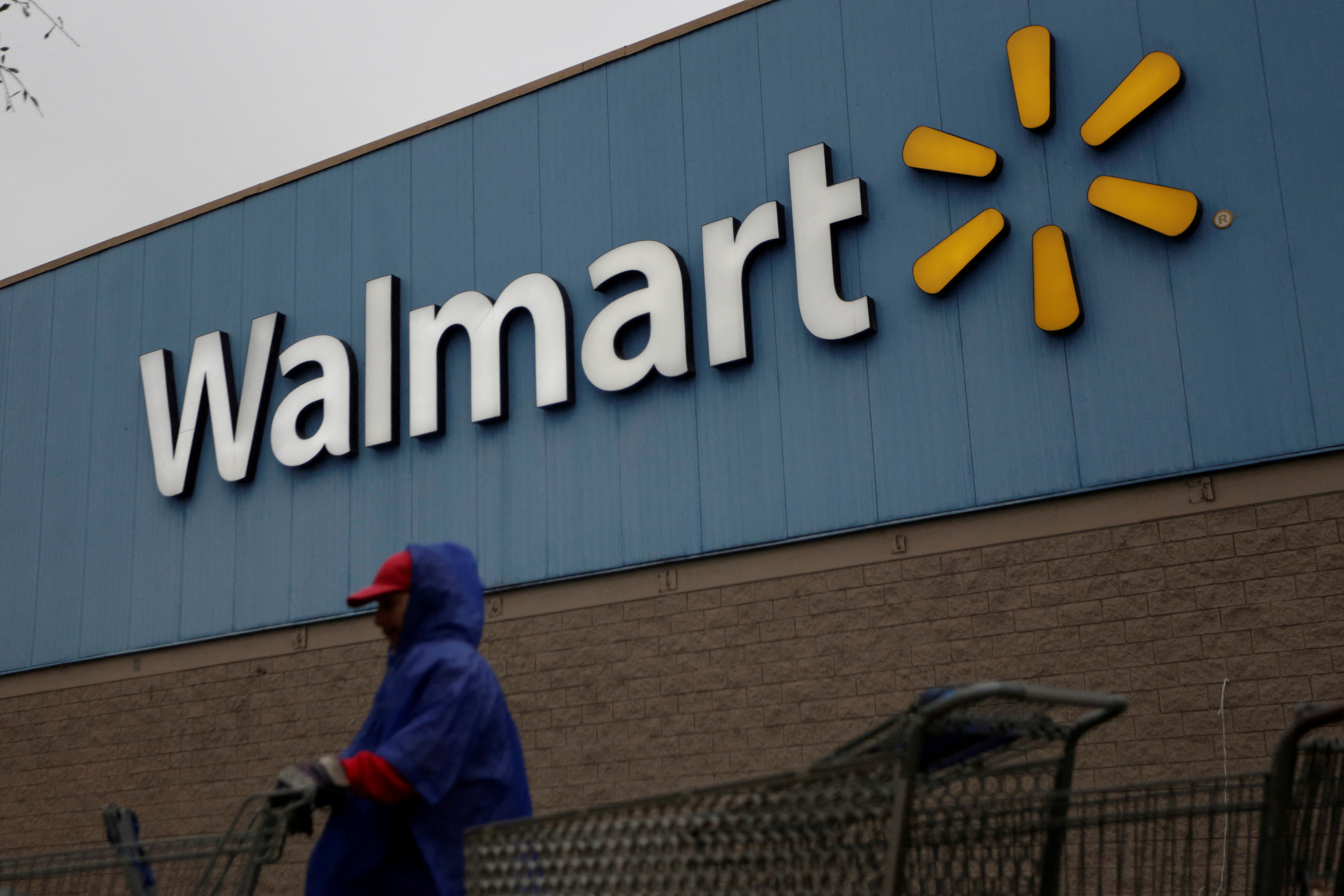Employee arranges shopping carts in front of the logo of Walmart outside a store in Monterrey