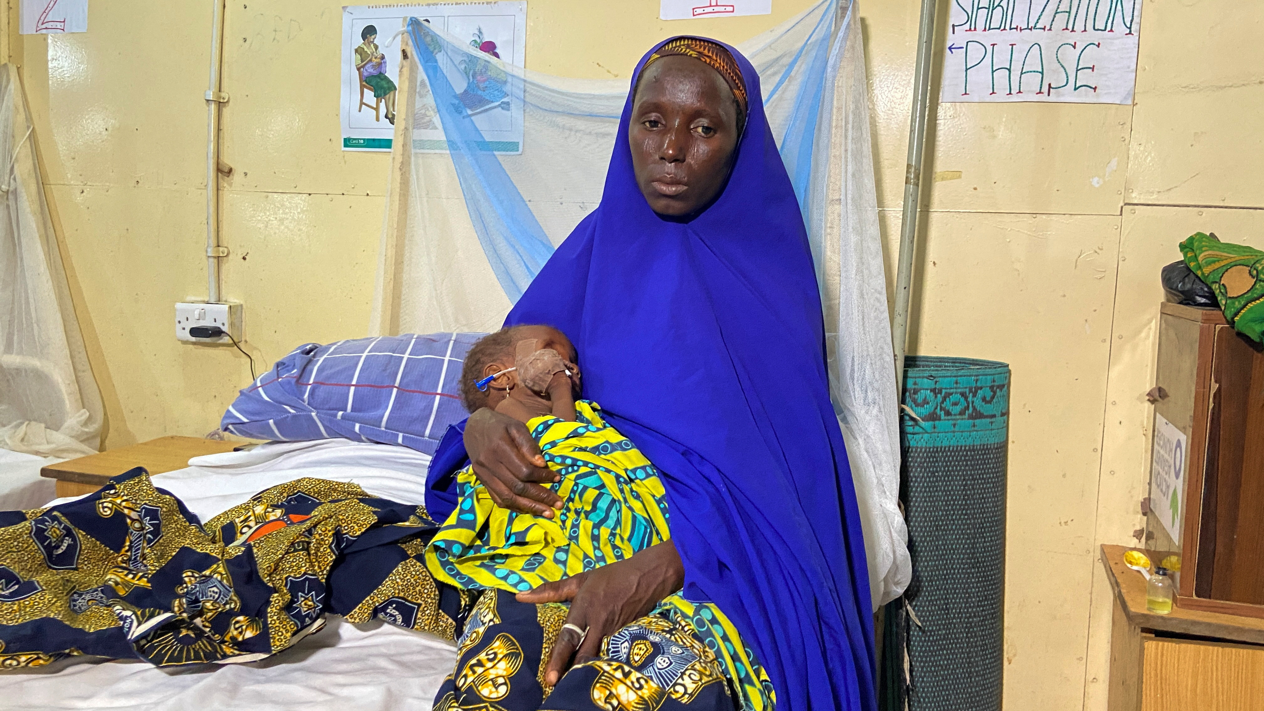 Fatima Usman carries her child, Aisha, as she sits on a bed in a treatment center for severely malnourished children in Damaturu, Yobe