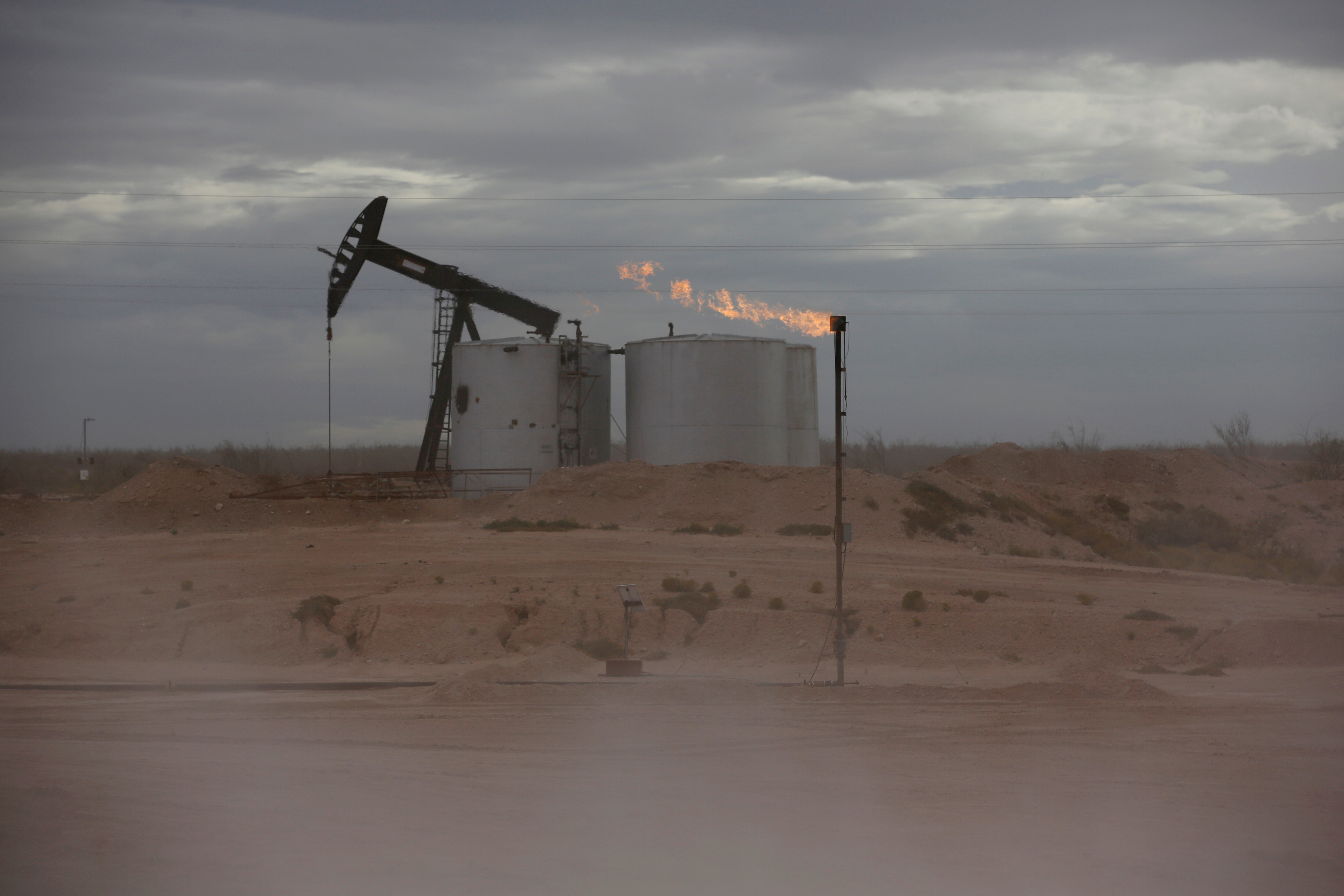 Dust blows around a crude oil pump jack and flare burning excess gas at a drill pad in the Permian Basin in Loving County, Texas, U.S. November 25, 2019.  REUTERS/Angus Mordant/File Photo