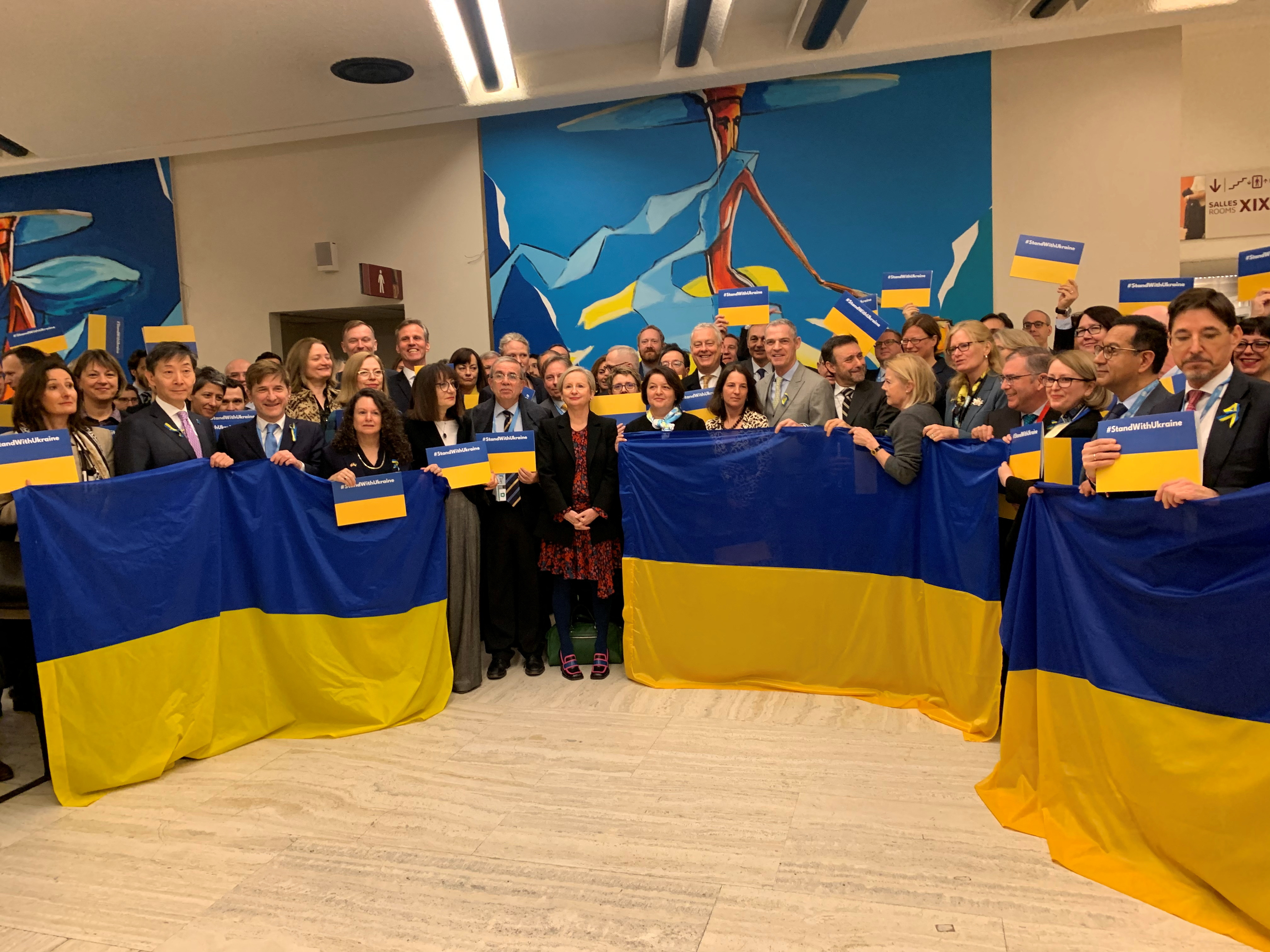 Ambassadors and delegates hold signs and flags in support of Ukraine during speech by Russian Deputy Foreign Minister Ryabkov in Geneva