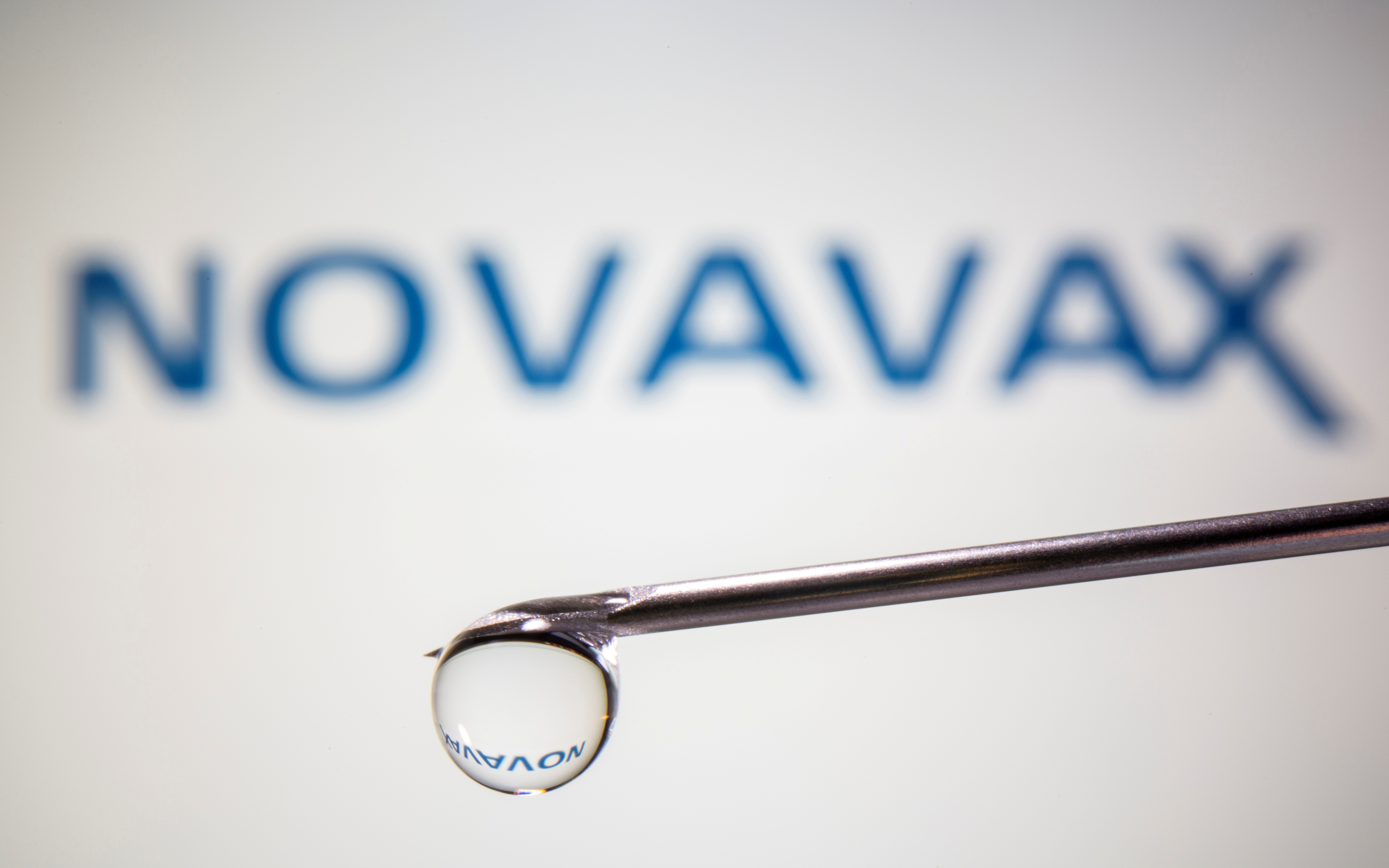A Novavax logo is reflected in a drop on a syringe needle in this illustration