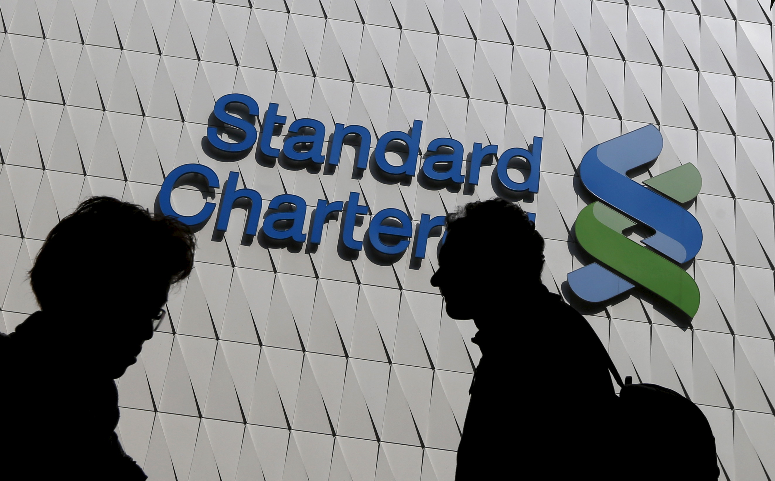 Passersby walk in front of the main branch of Standard Chartered in Hong Kong, January 8, 2015. REUTERS/Bobby Yip/File Photo