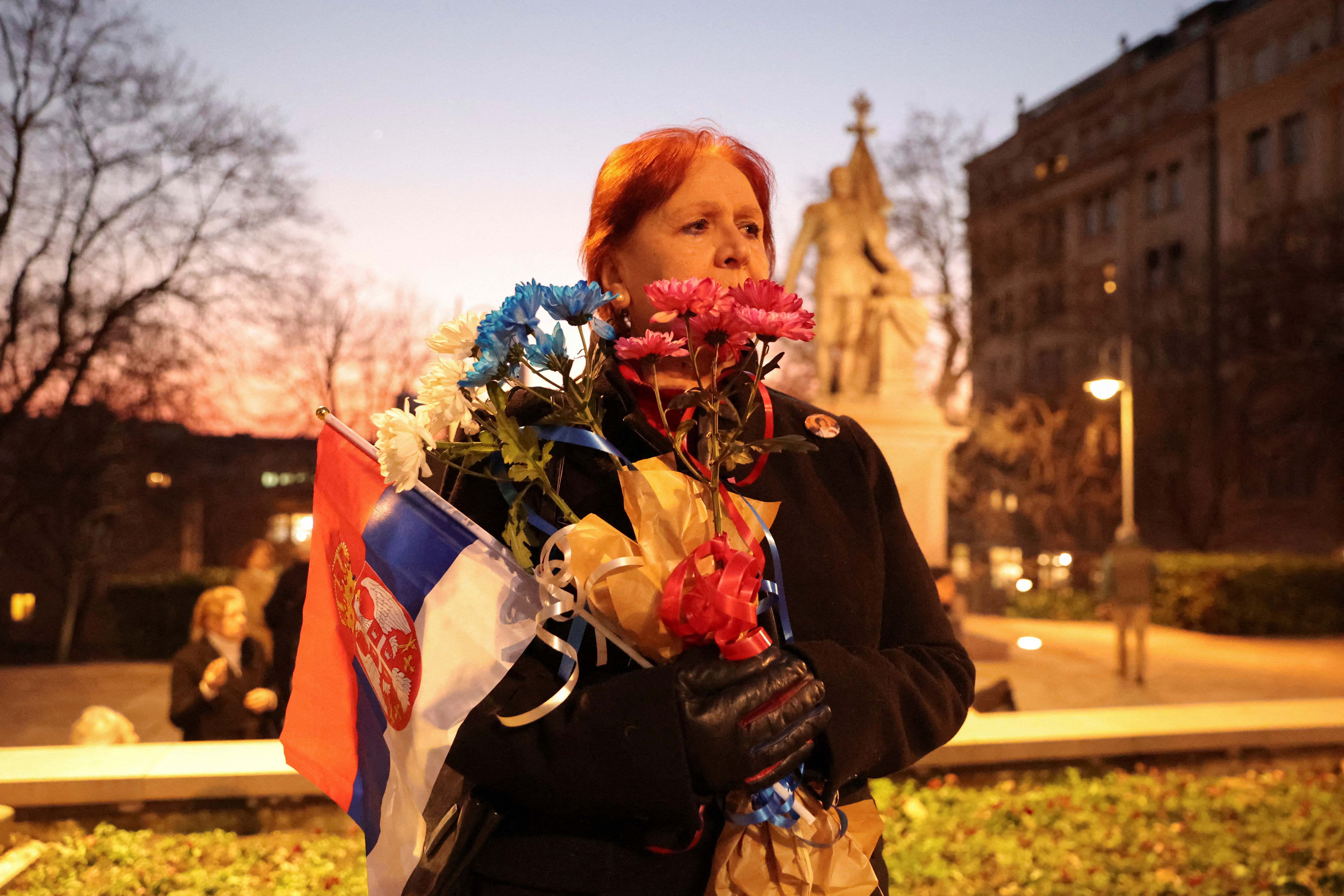 A woman holds an Serbian flag and flowers in colours of Russian flag during a protest against the Serbian authorities and French-German plan for the resolution of Kosovo