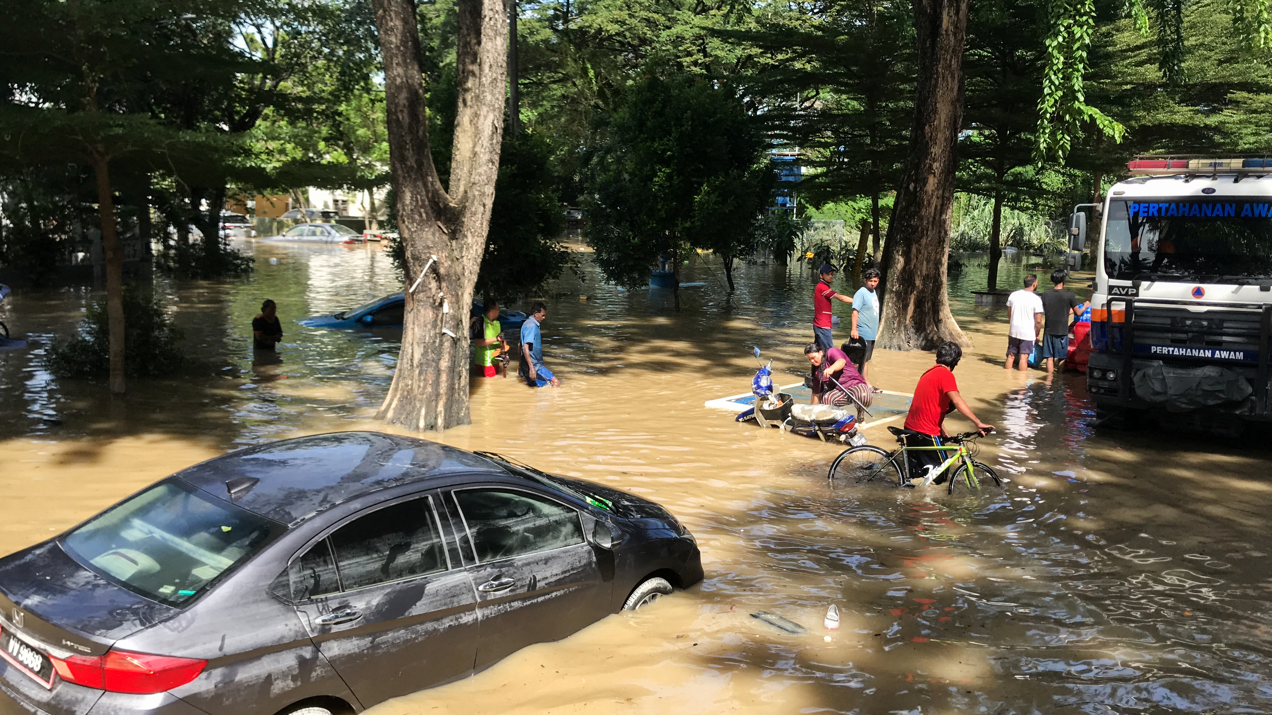 People wade among partially submerged vehicles through flood waters in Shah Alam