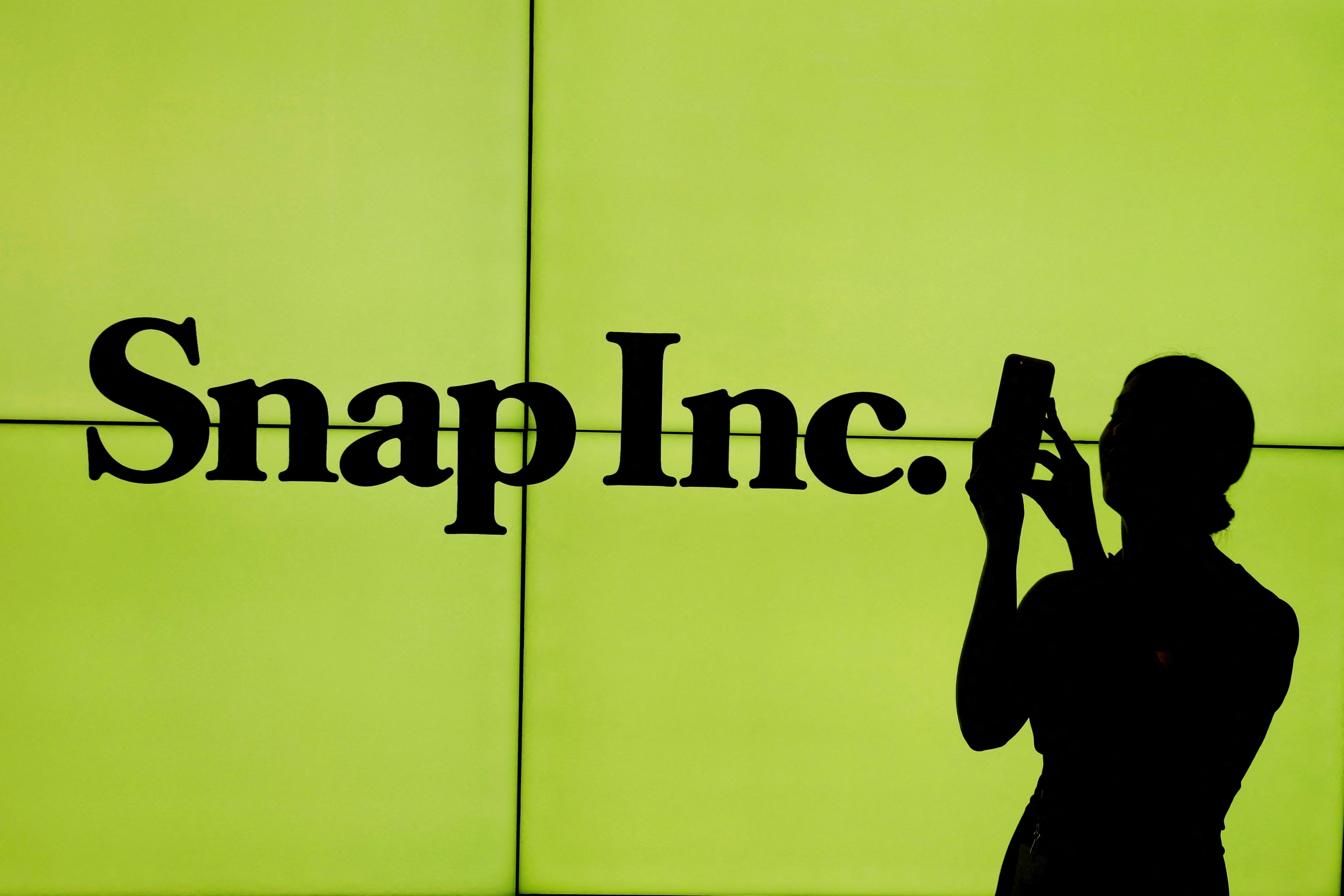A woman stands in front of the logo of Snap Inc. on the floor of the New York Stock Exchange in New York City