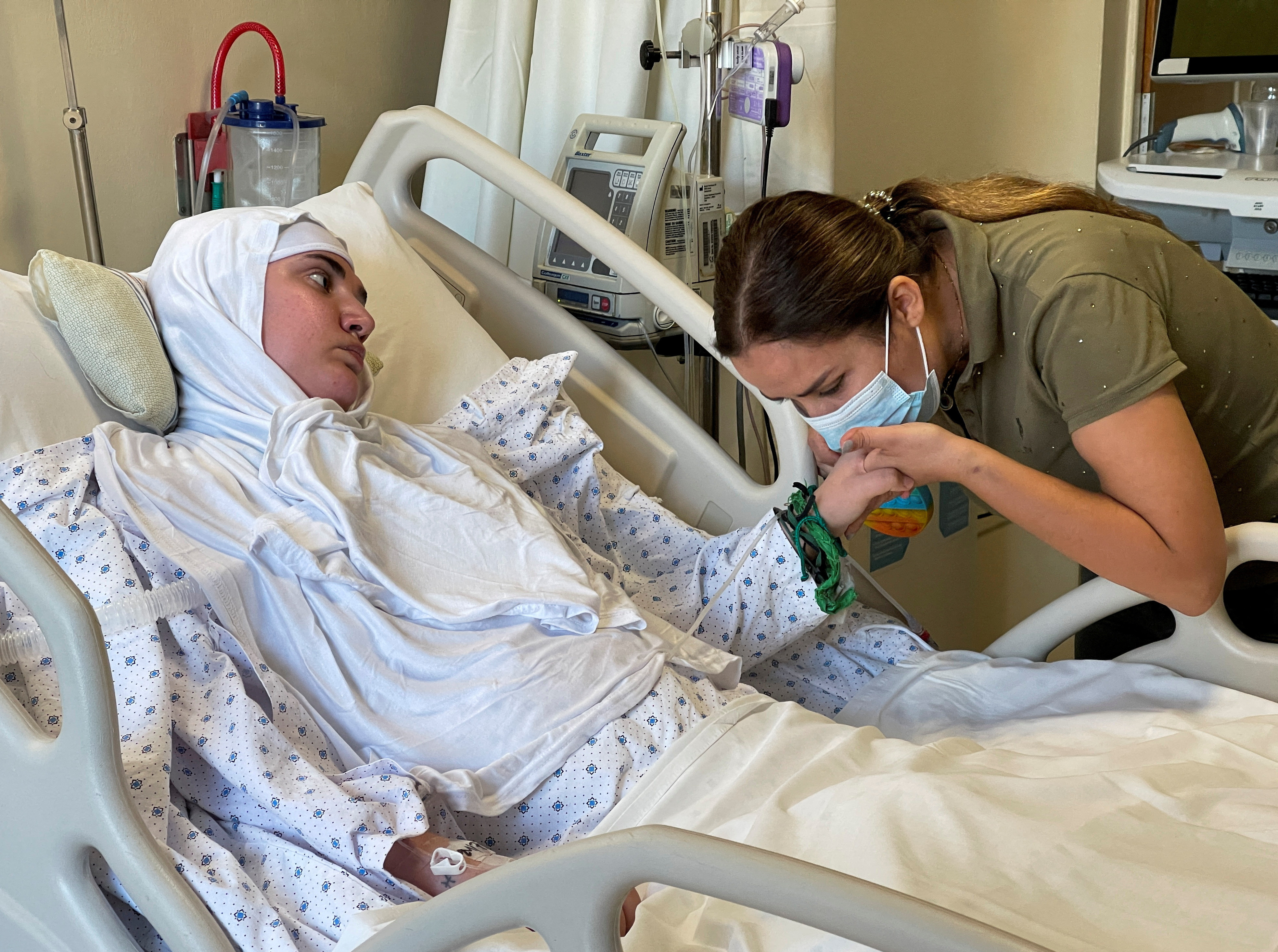 Nassma Cheaito, kisses the hand of her sister, Liliane who is mostly paralyzed from August 2020 port as she lies on hospital bed at the American University of Beirut Medical Center (AUBMC) in Beirut