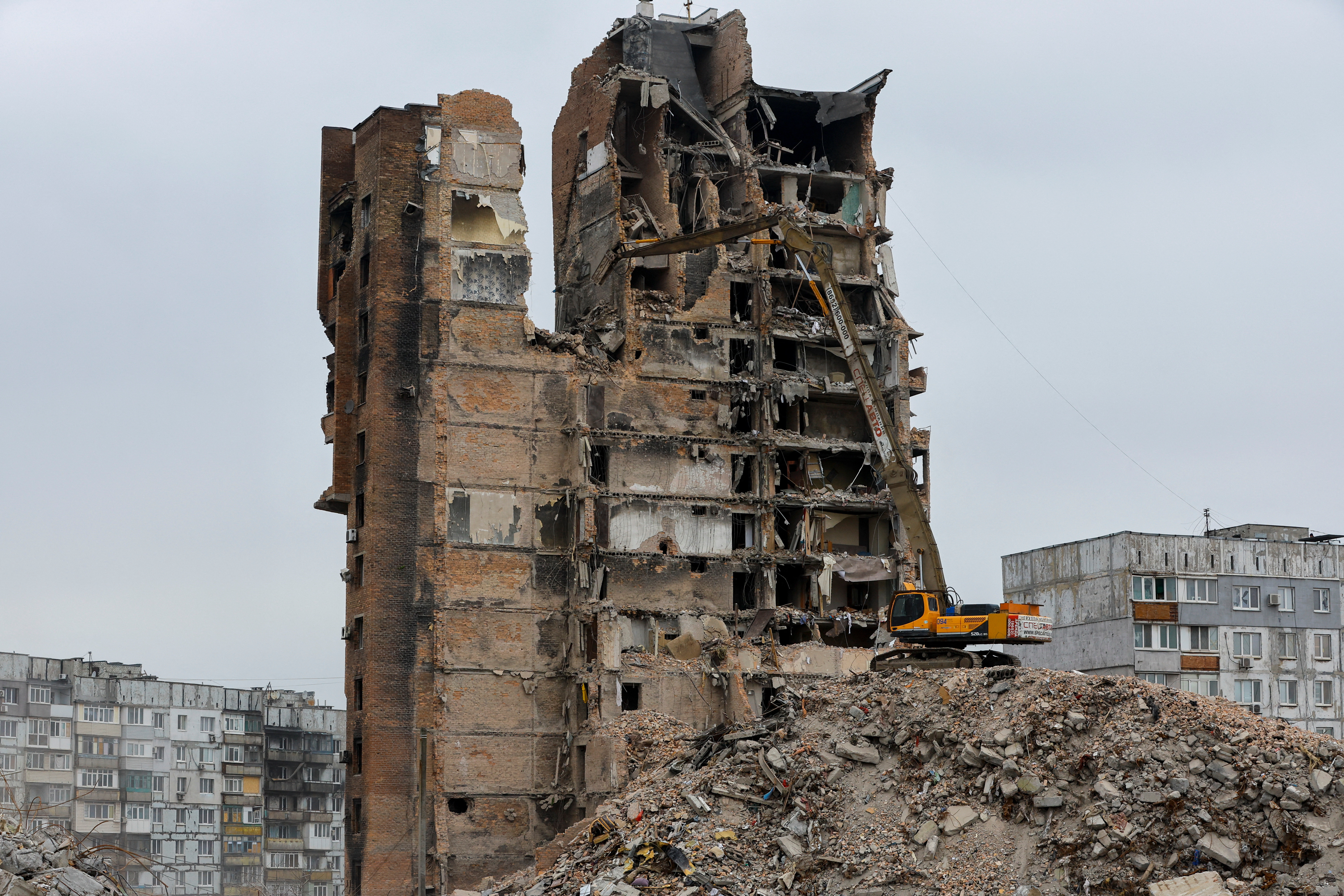 An excavator demolishes a multi-storey apartment block in Mariupol