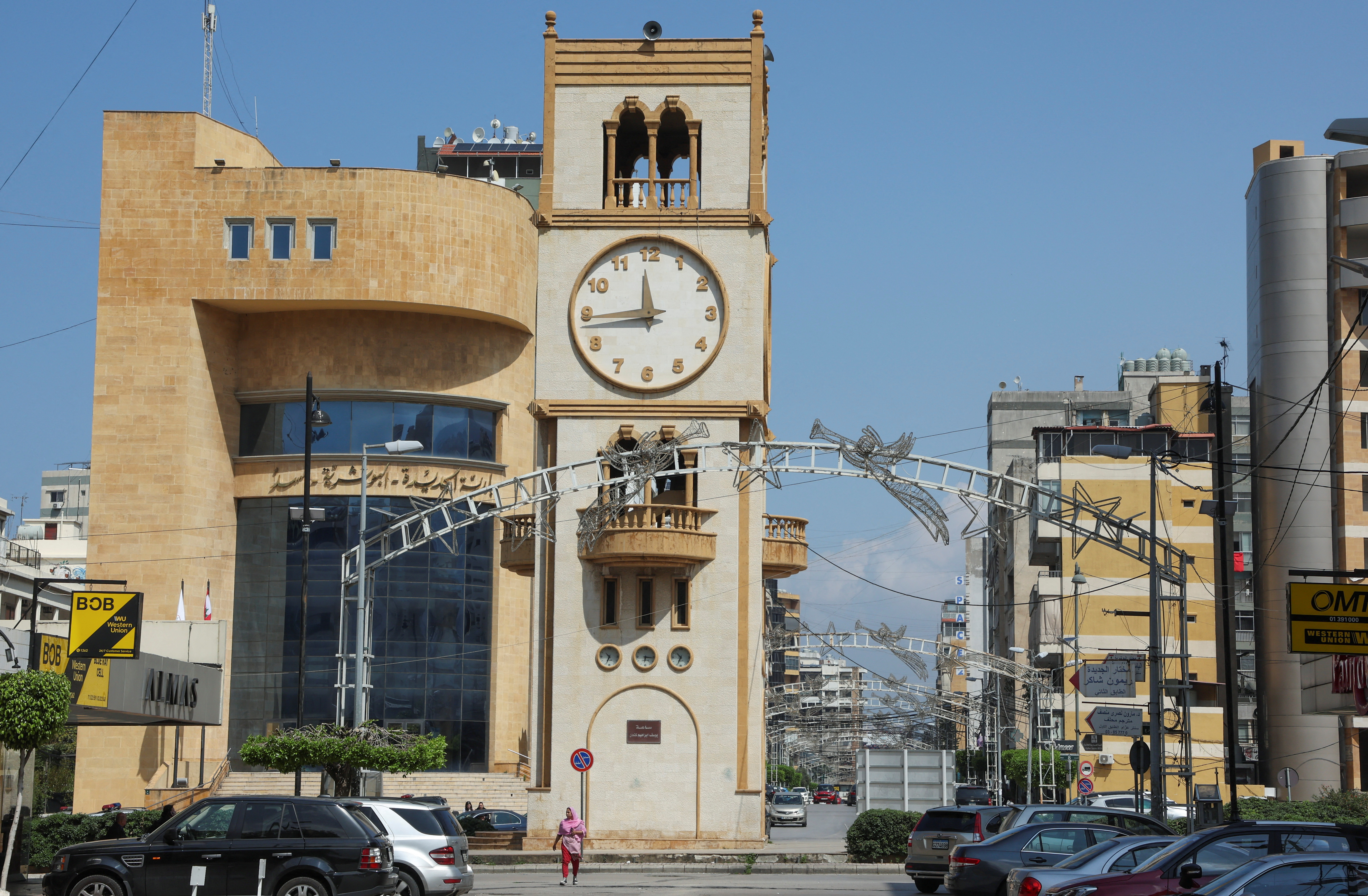 A woman walks near a clock tower that indicates the time in Jdeideh