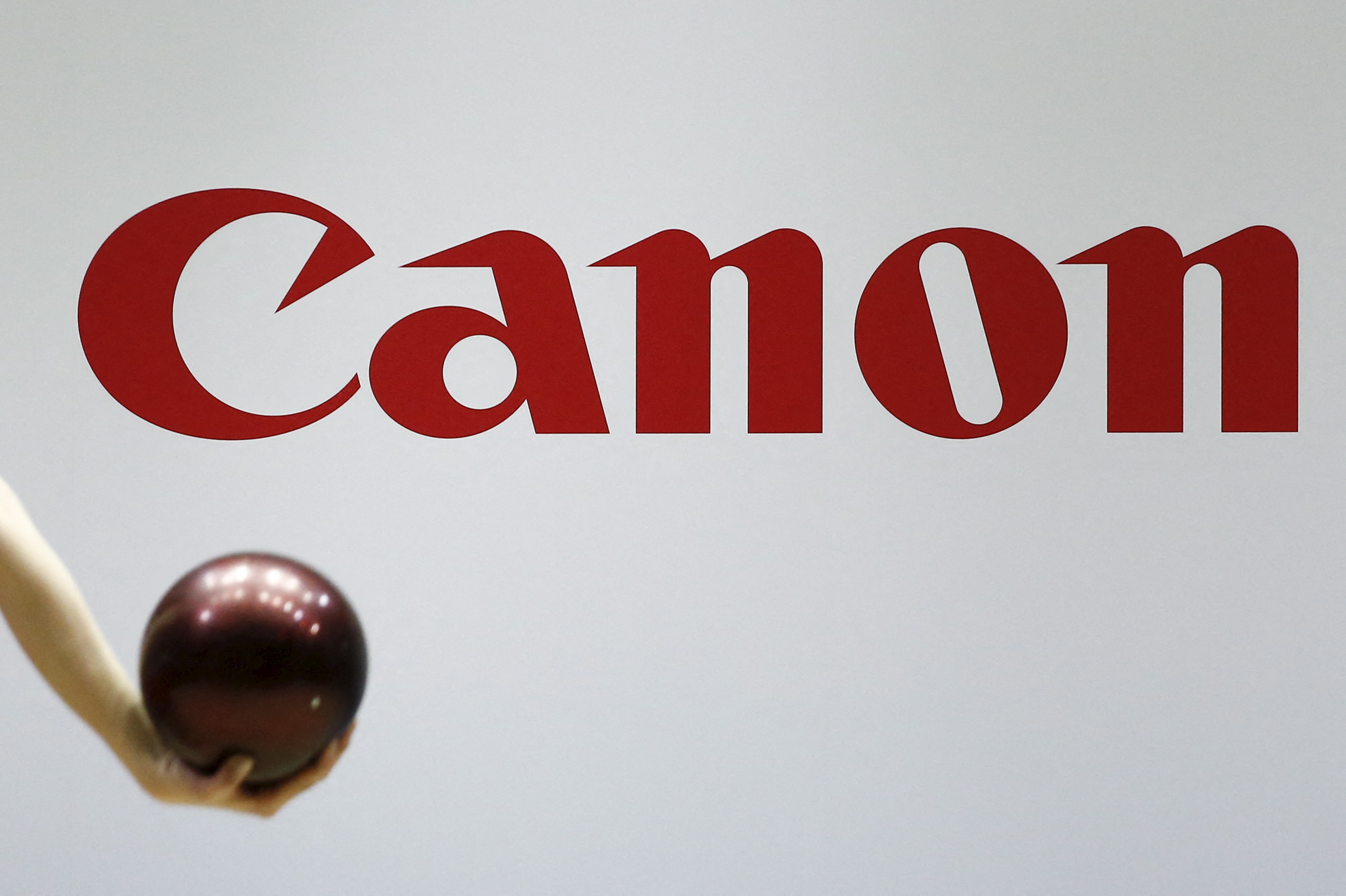 A gymnast performs in front of the Canon brand logo at the Canon stall at CP+ camera and photo trade fair in Yokohama