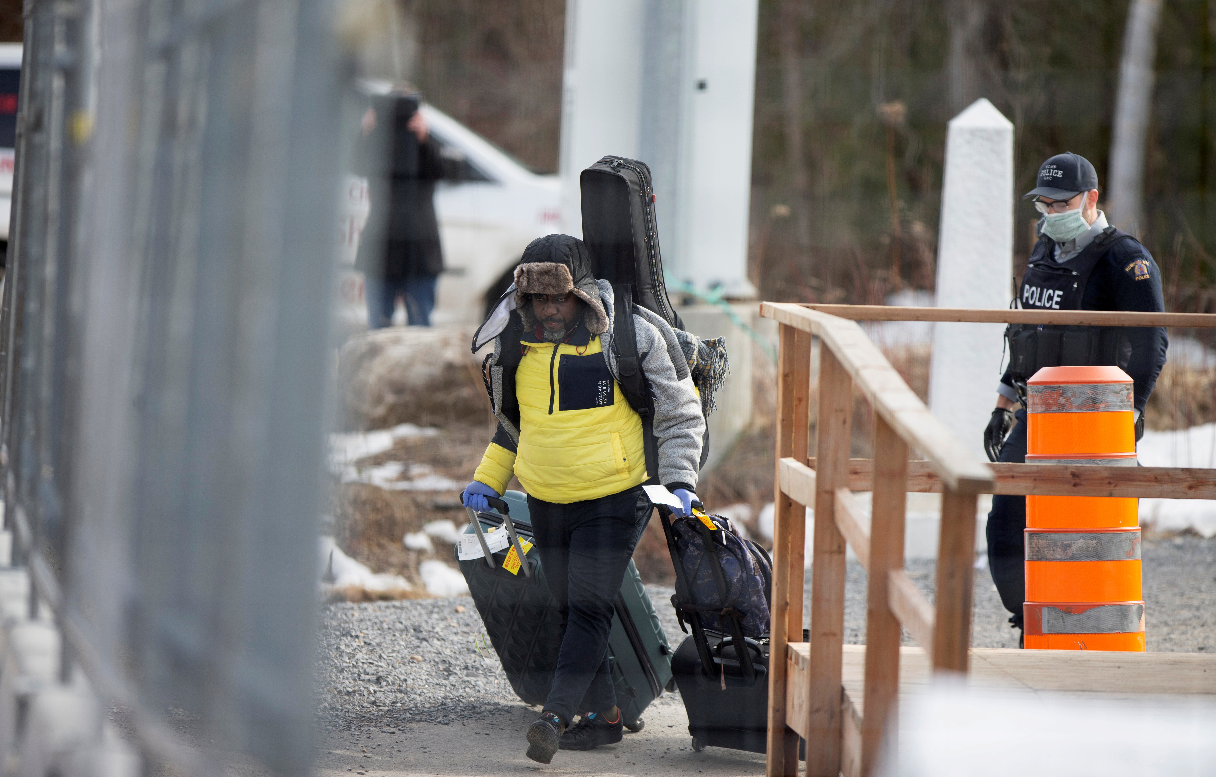 An asylum seeker crosses the border from New York into Canada followed by a Royal Canadian Mounted Police (RCMP) officer at Roxham Road in Hemmingford, Quebec, Canada March 18, 2020.  REUTERS/Christinne Muschi/File Photo