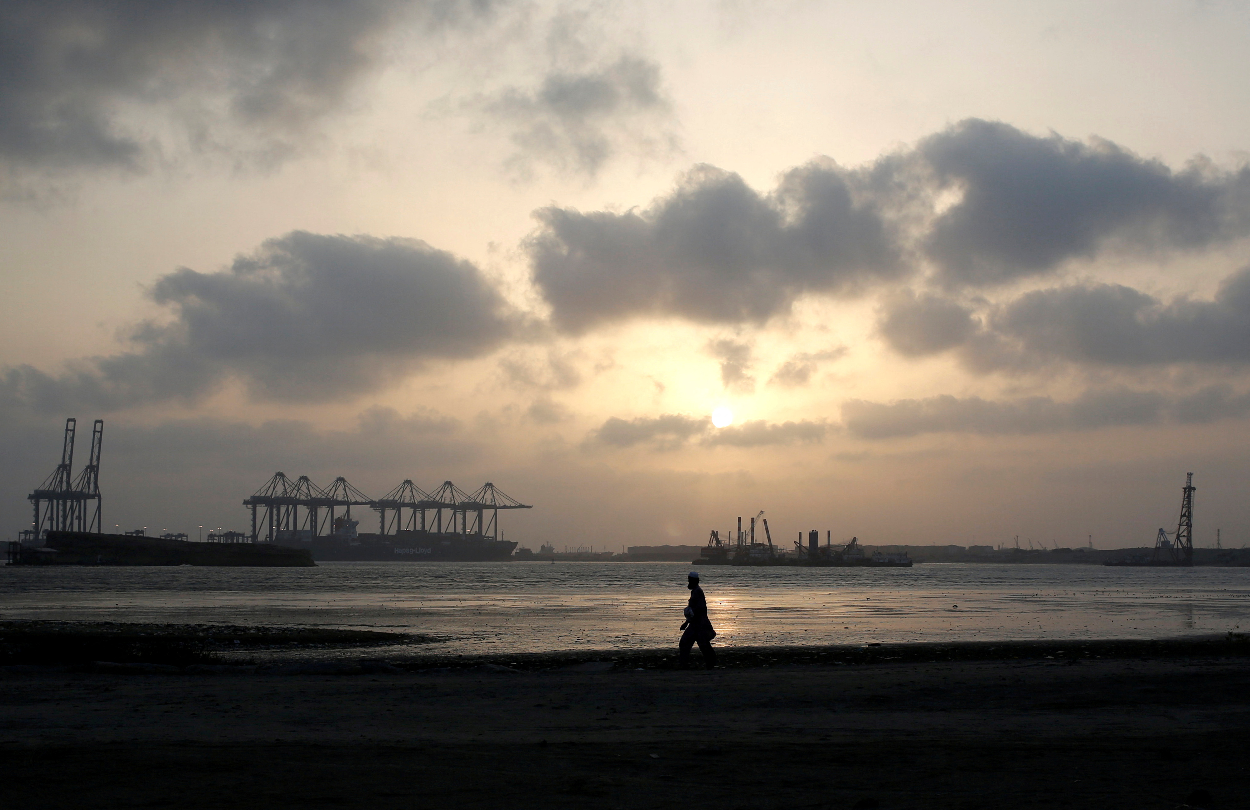 A man is silhouetted as he walks amid hot and humid weather at breakwater along port area in Karachi