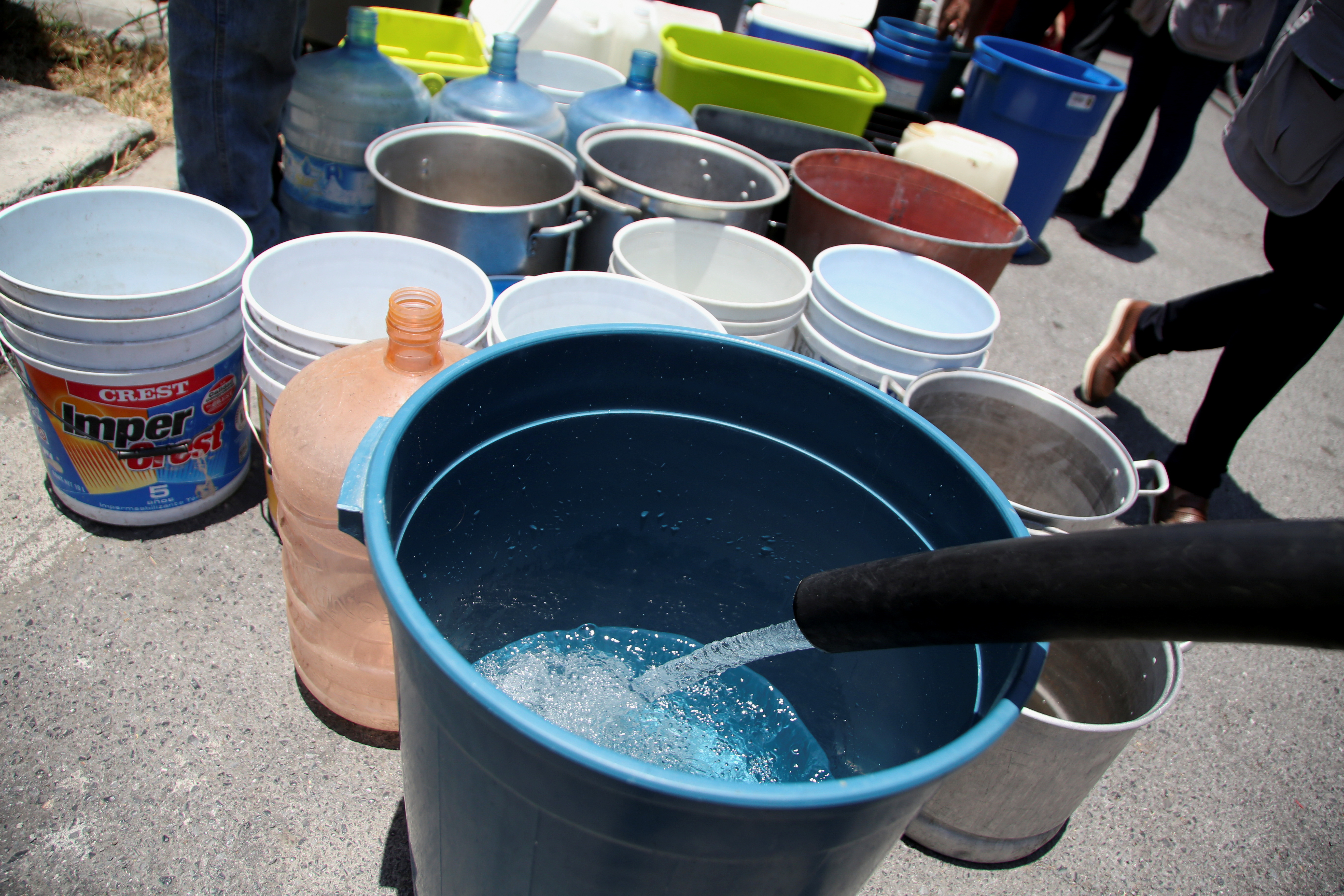 Buckets are refilled with water by residents as a water truck distributes it outside houses at La Hacienda neighborhood in Guadalupe