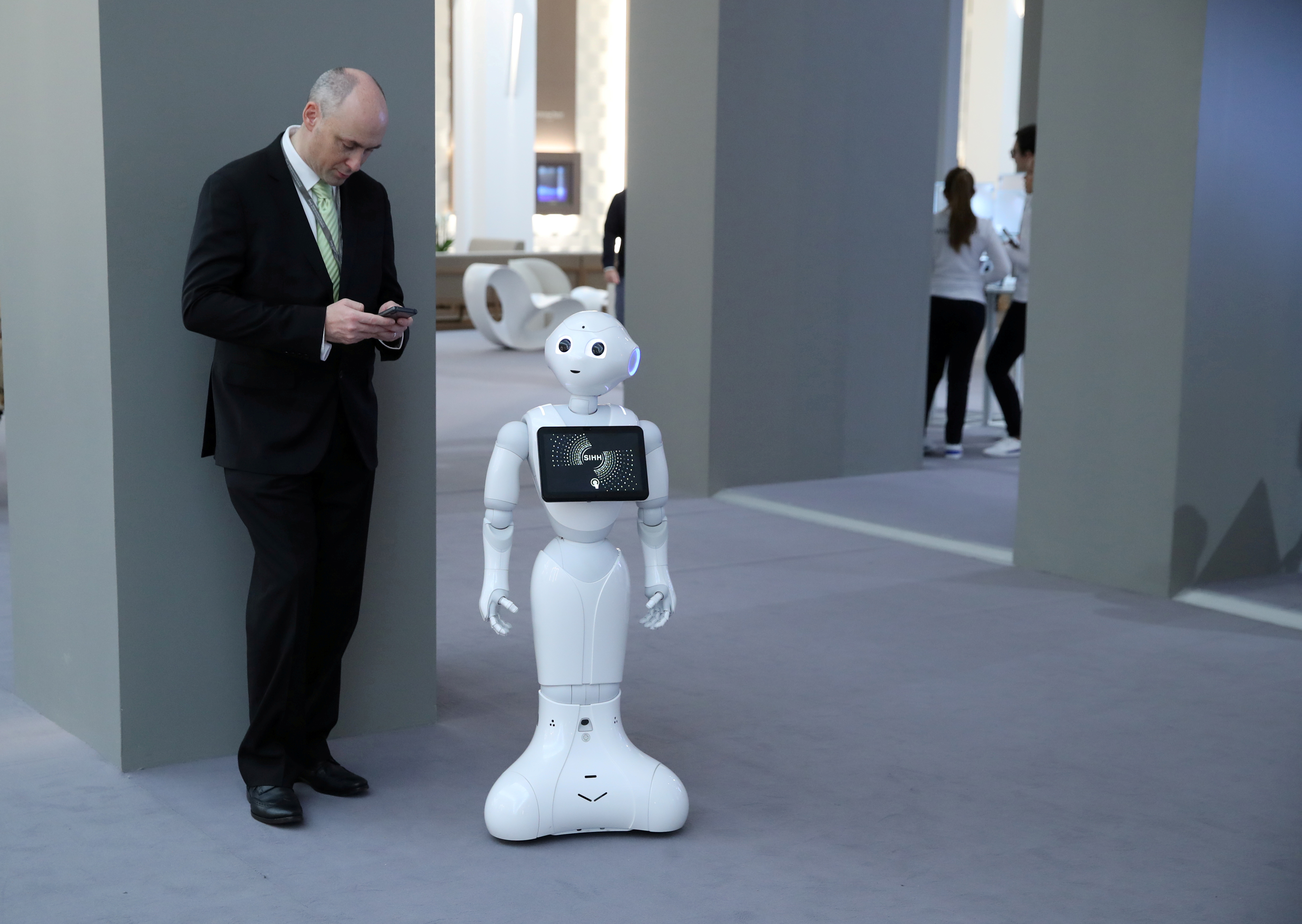 A visitor looks at his mobile device next to Pepper the robot during the 
