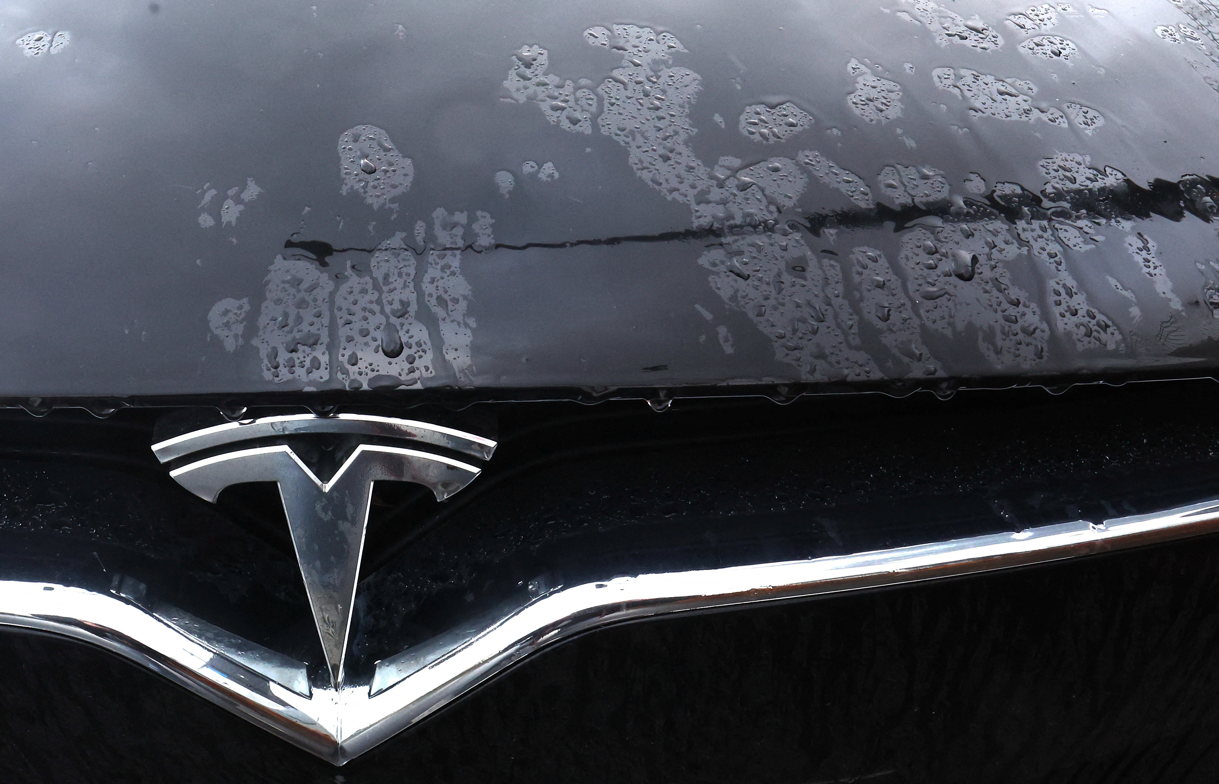 The logo of a Tesla electric vehicle is seen on a car seen outside a dealership in Drogenbos