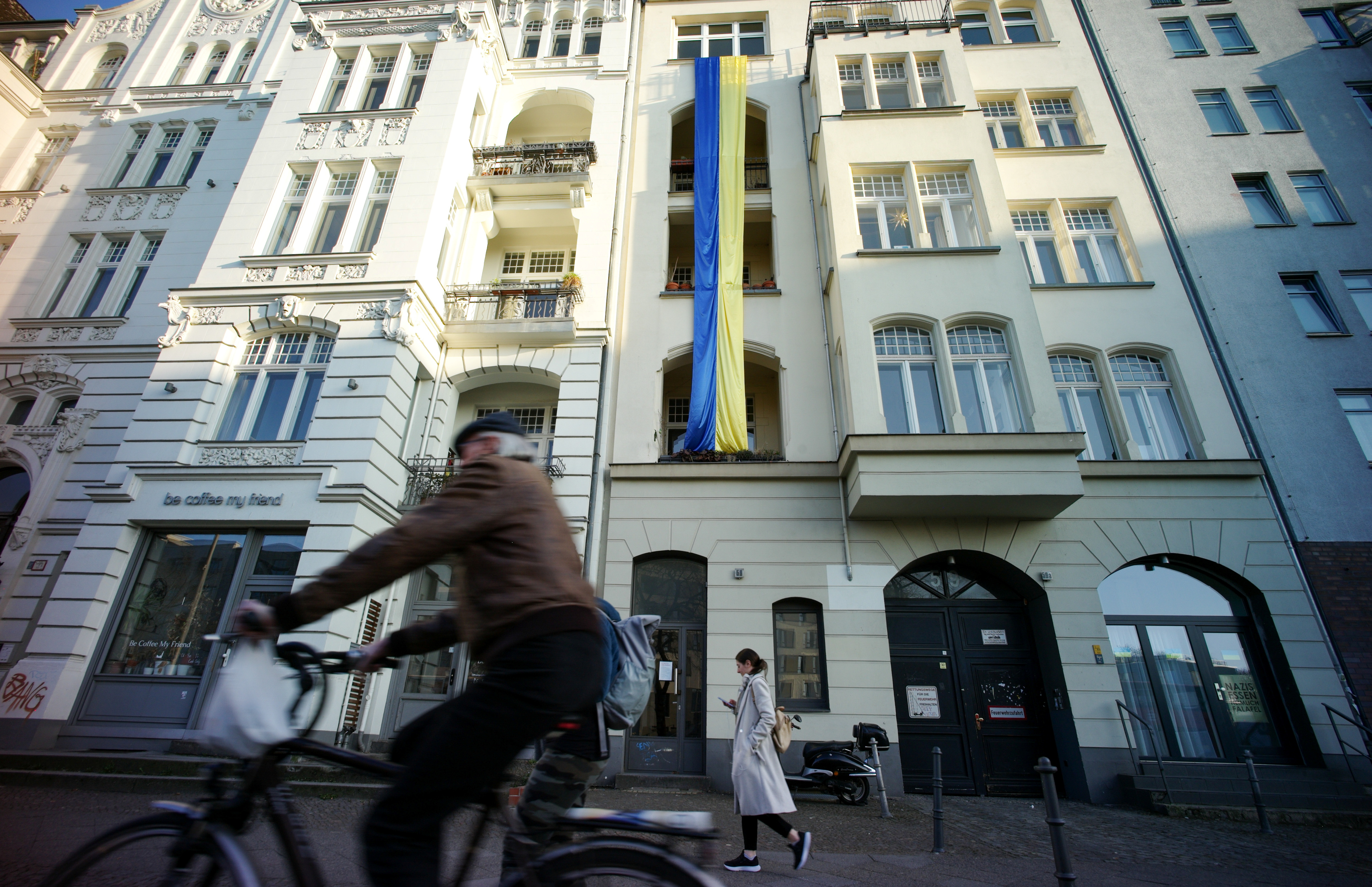 Pedestrians walk past a Ukrainian flag hanging in support of the country on an apartment building in Berlin